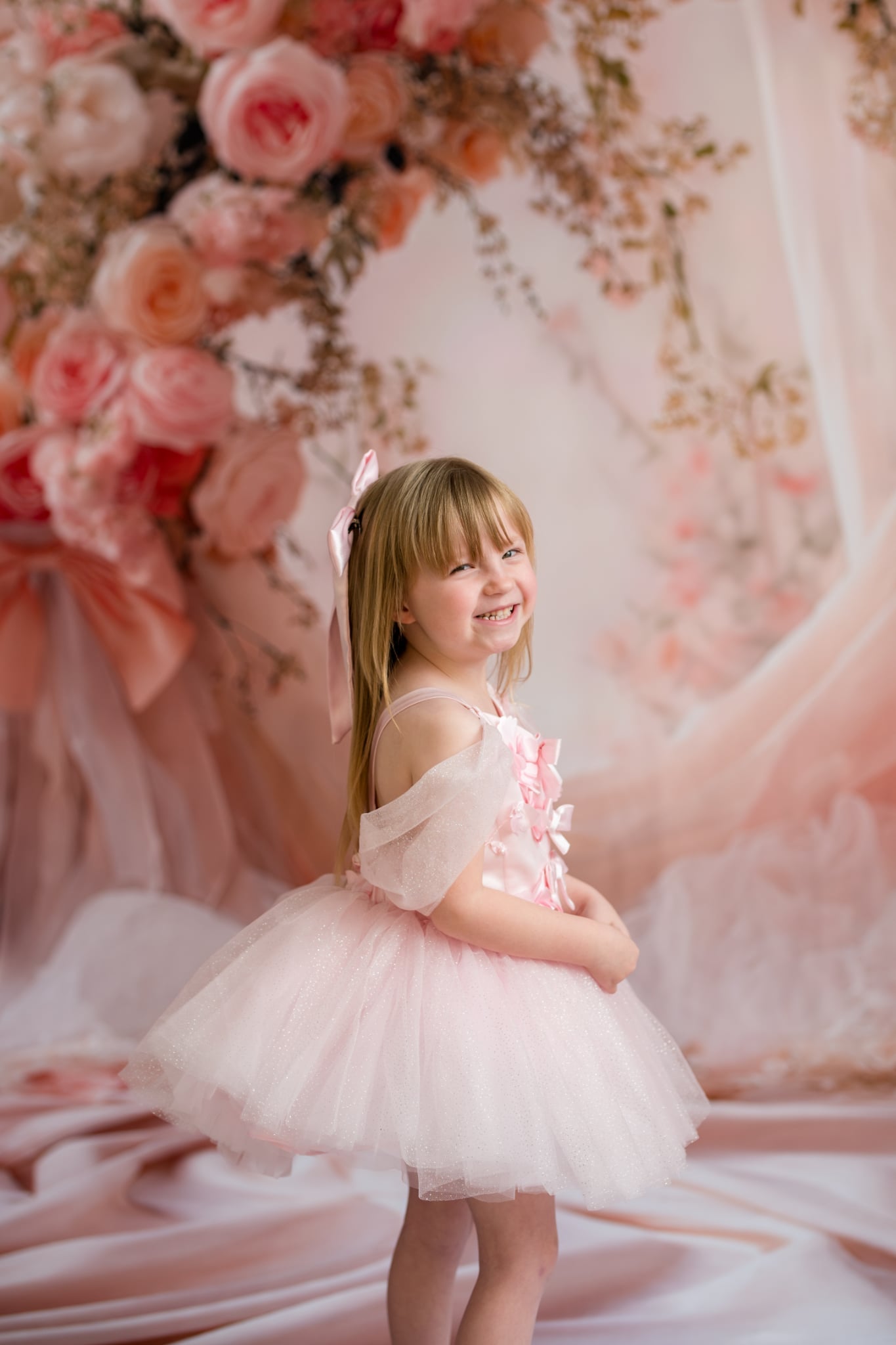 Young girl in a pink dress standing in front of a floral backdrop
