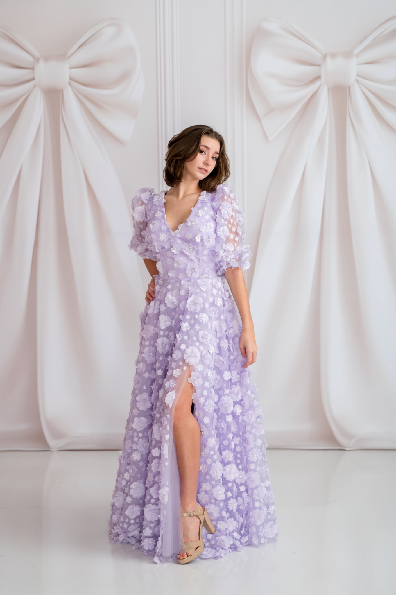 Woman wearing a purple floral dress against a white background with large bows.