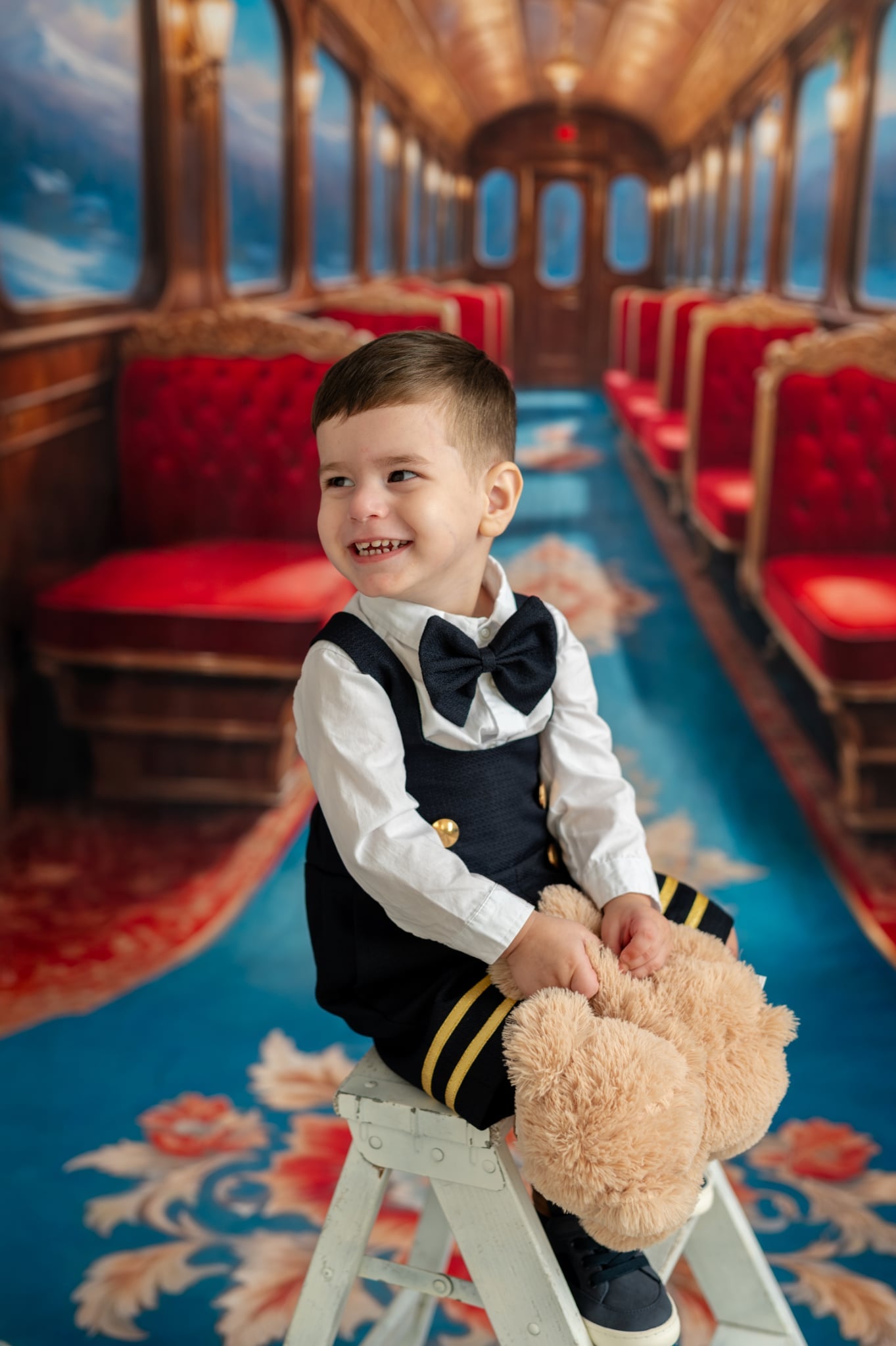 Child in a formal outfit with a teddy bear on a decorative train car.