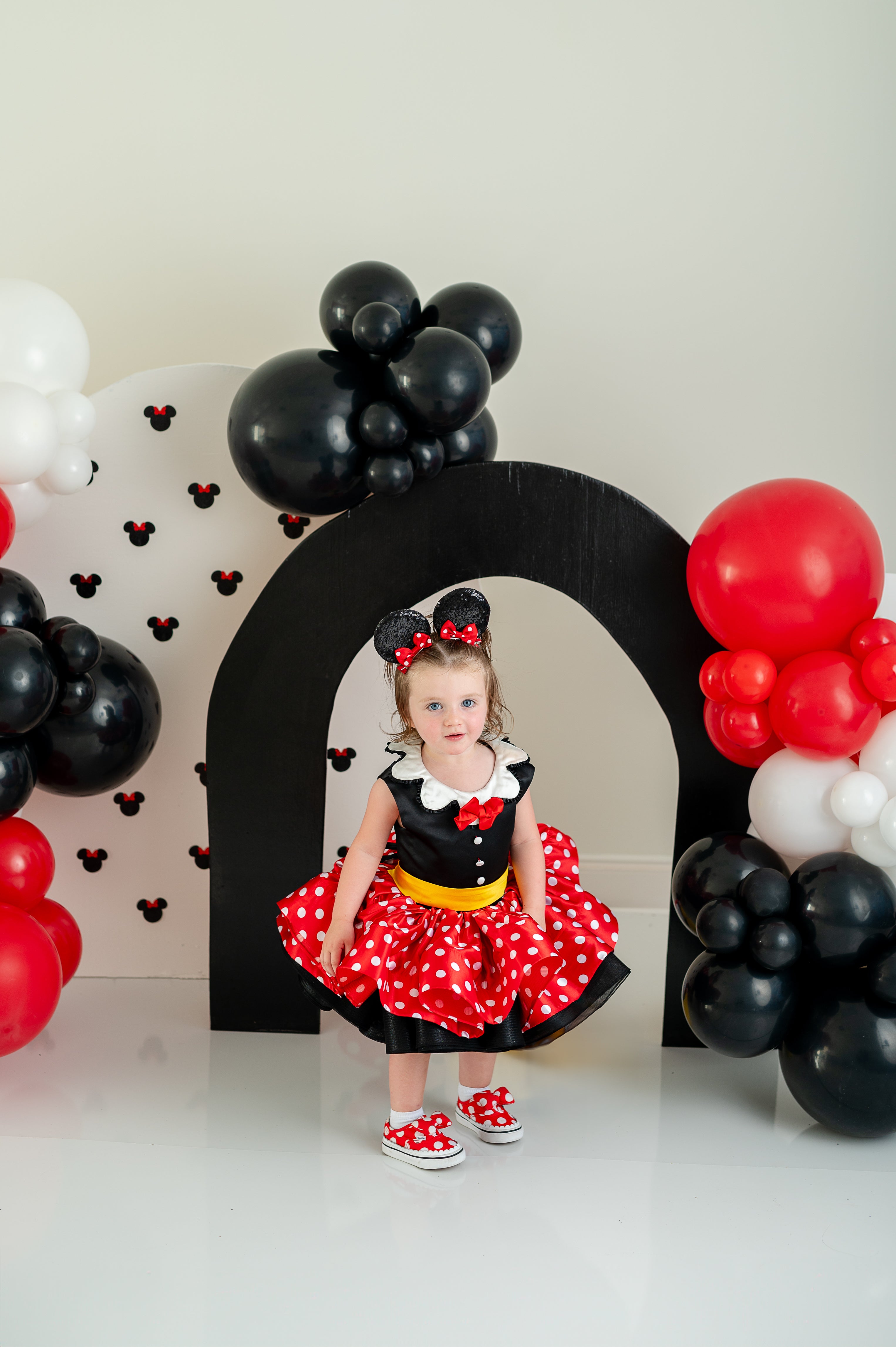 "Charming Minnie Mouse-inspired dress in red with white polka dots, featuring a black bow detail and puffed sleeves for a playful Disney look."