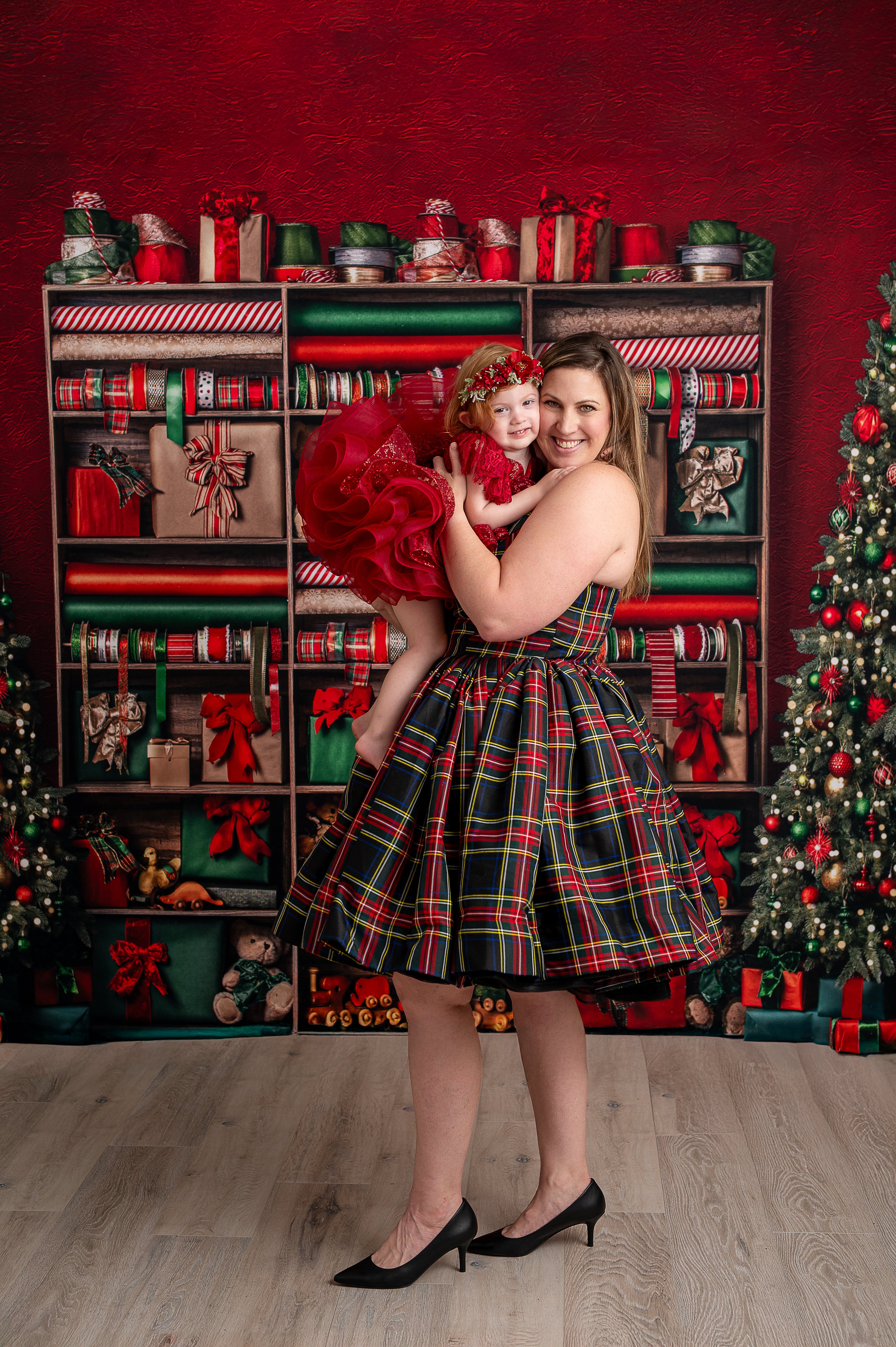 Holiday family photography with mom and children in coordinating red, green, and plaid outfits, Christmas-themed background.