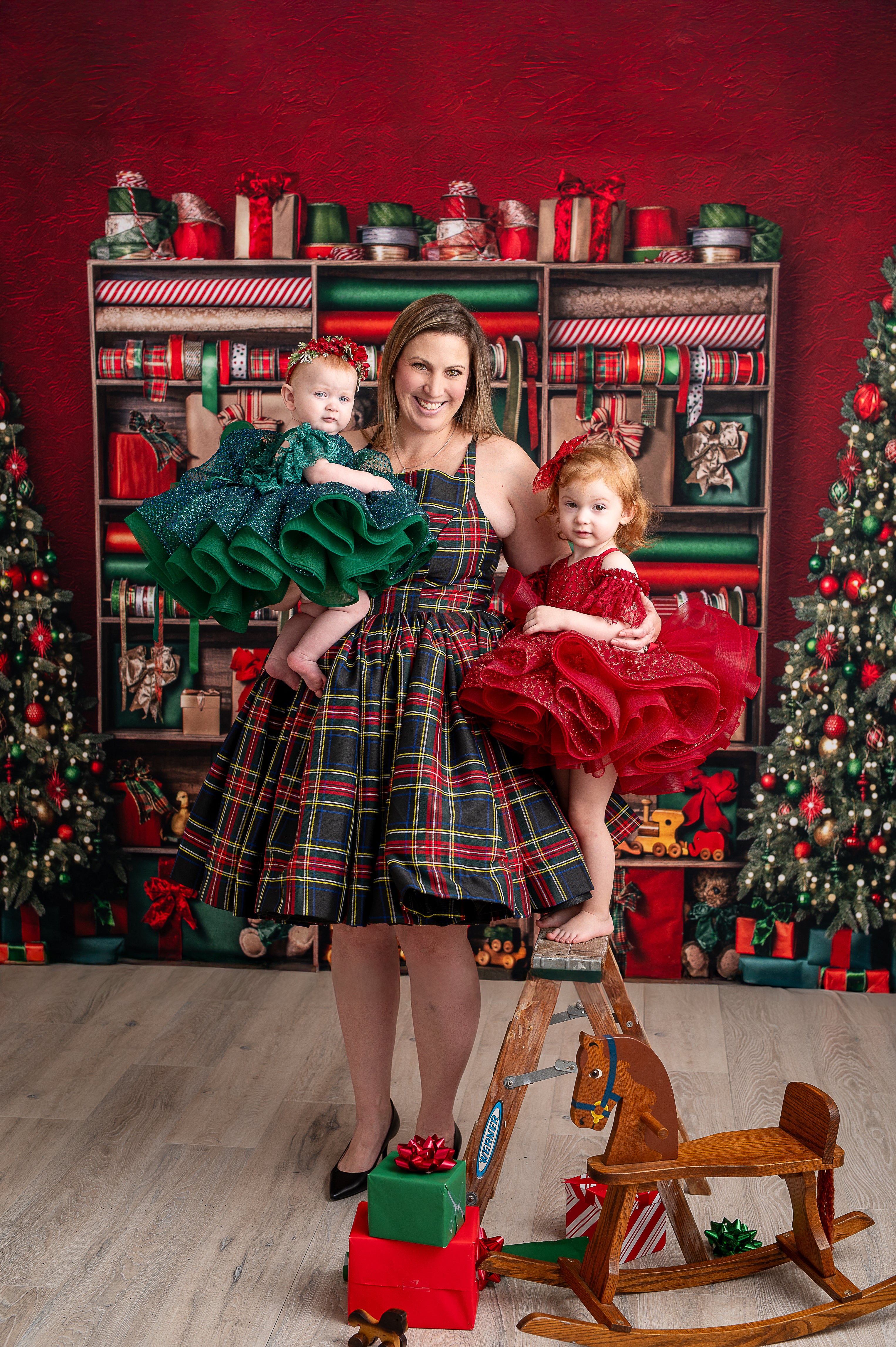 Festive mother-daughter Christmas portrait with plaid dress, green and red holiday outfits, and holiday backdrop.