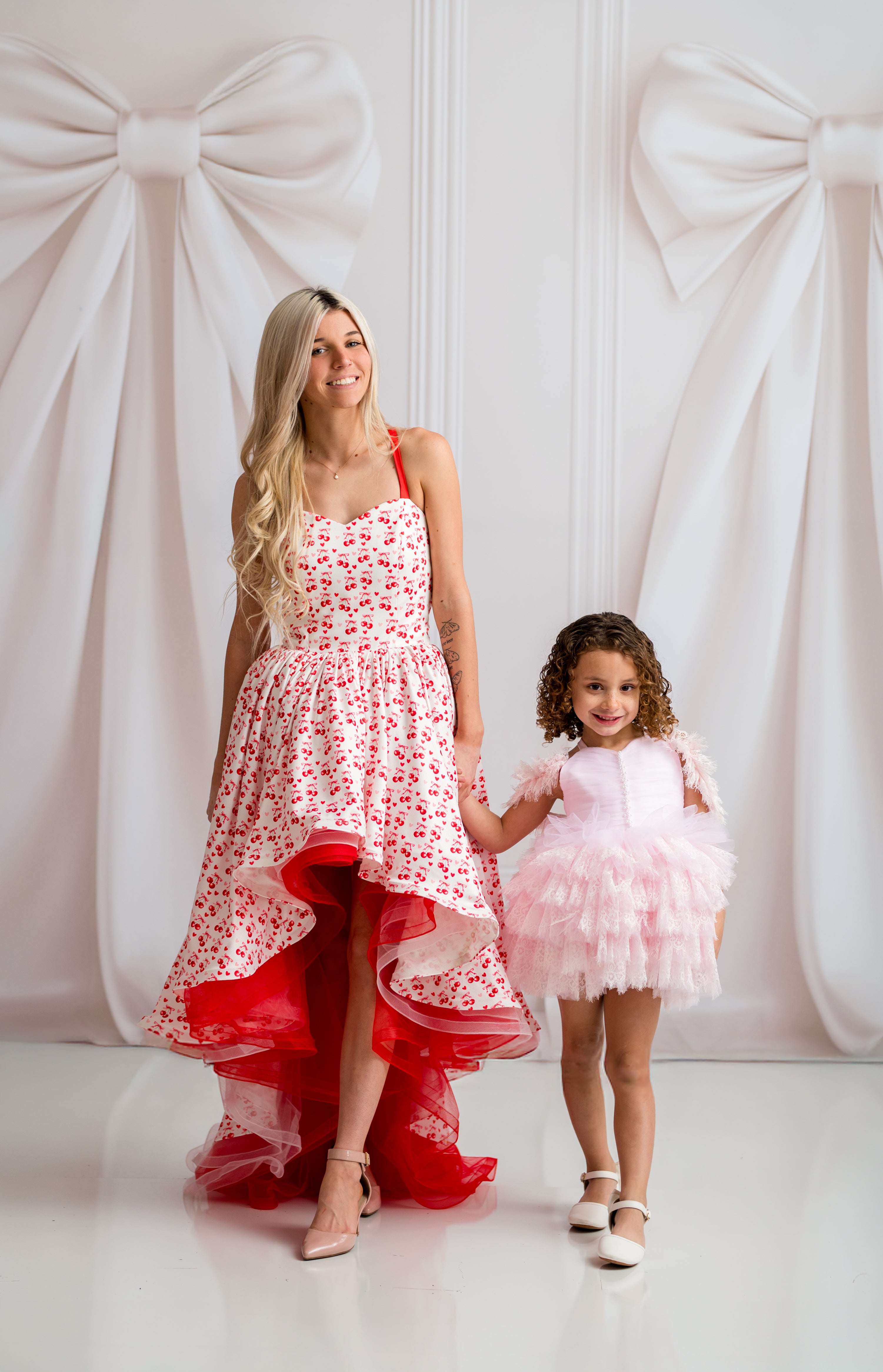 Woman and child in matching dresses standing against a white background with decorative bows.