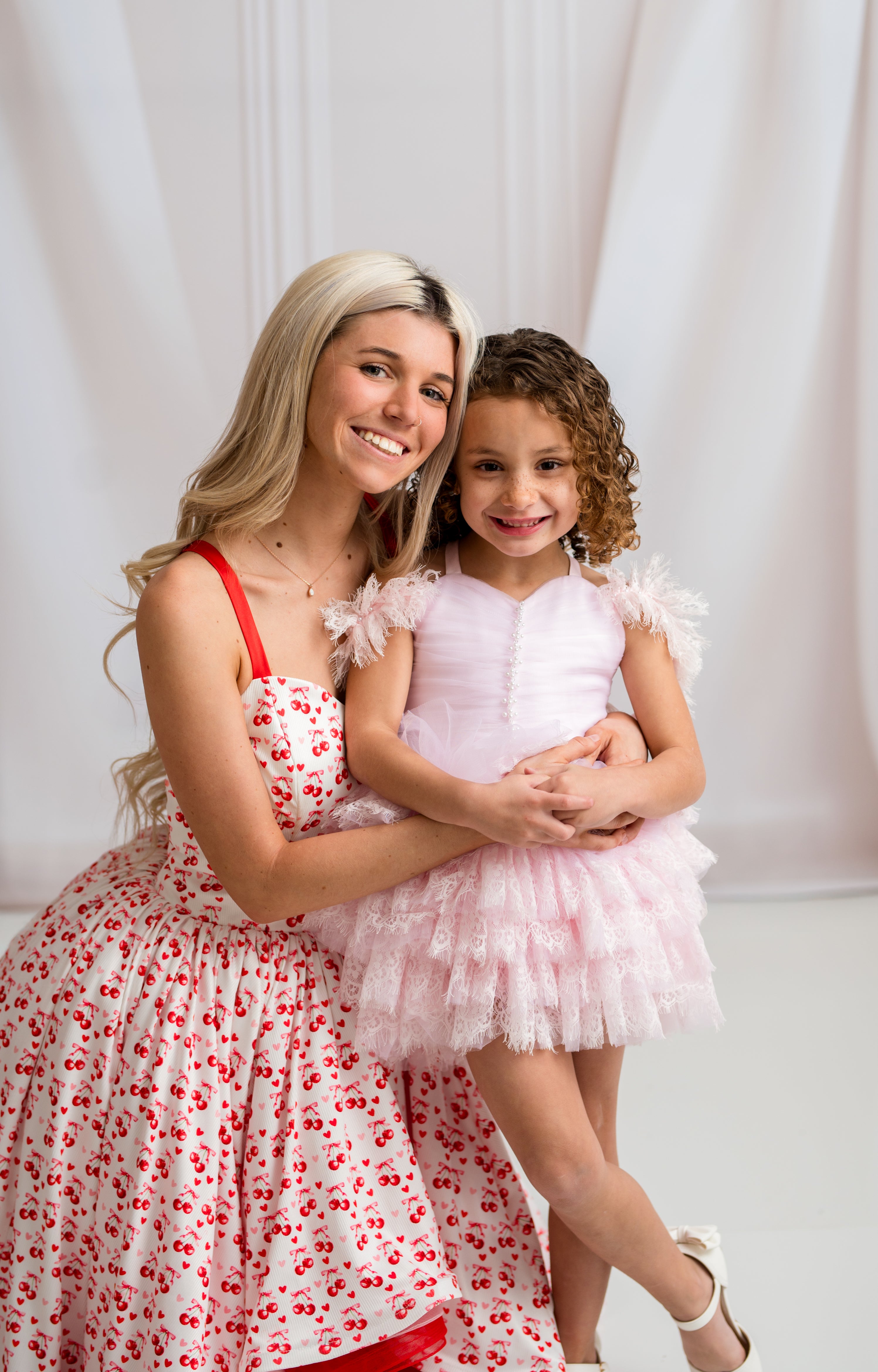 Woman and young girl in floral dresses posing against a white curtain