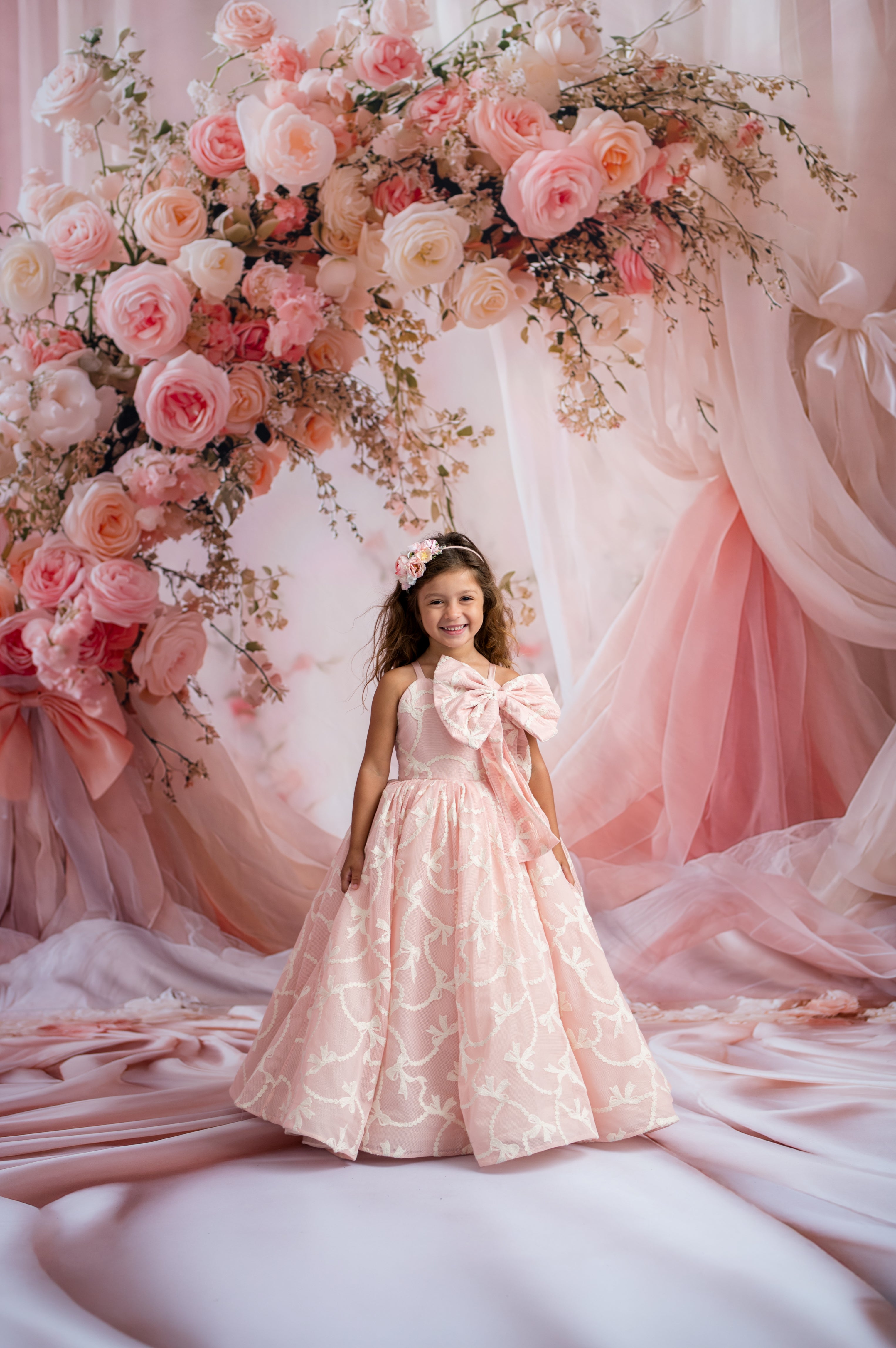 Young girl in a pink dress standing in front of a floral arch with pink and white flowers.