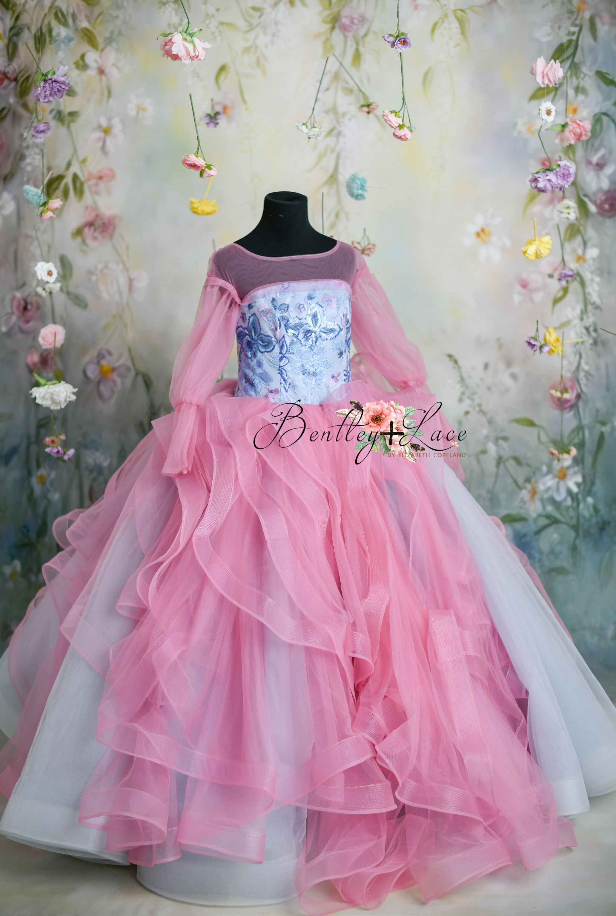 Fairy-tale-inspired pink ruffled gown with floral embroidery and sheer sleeves.