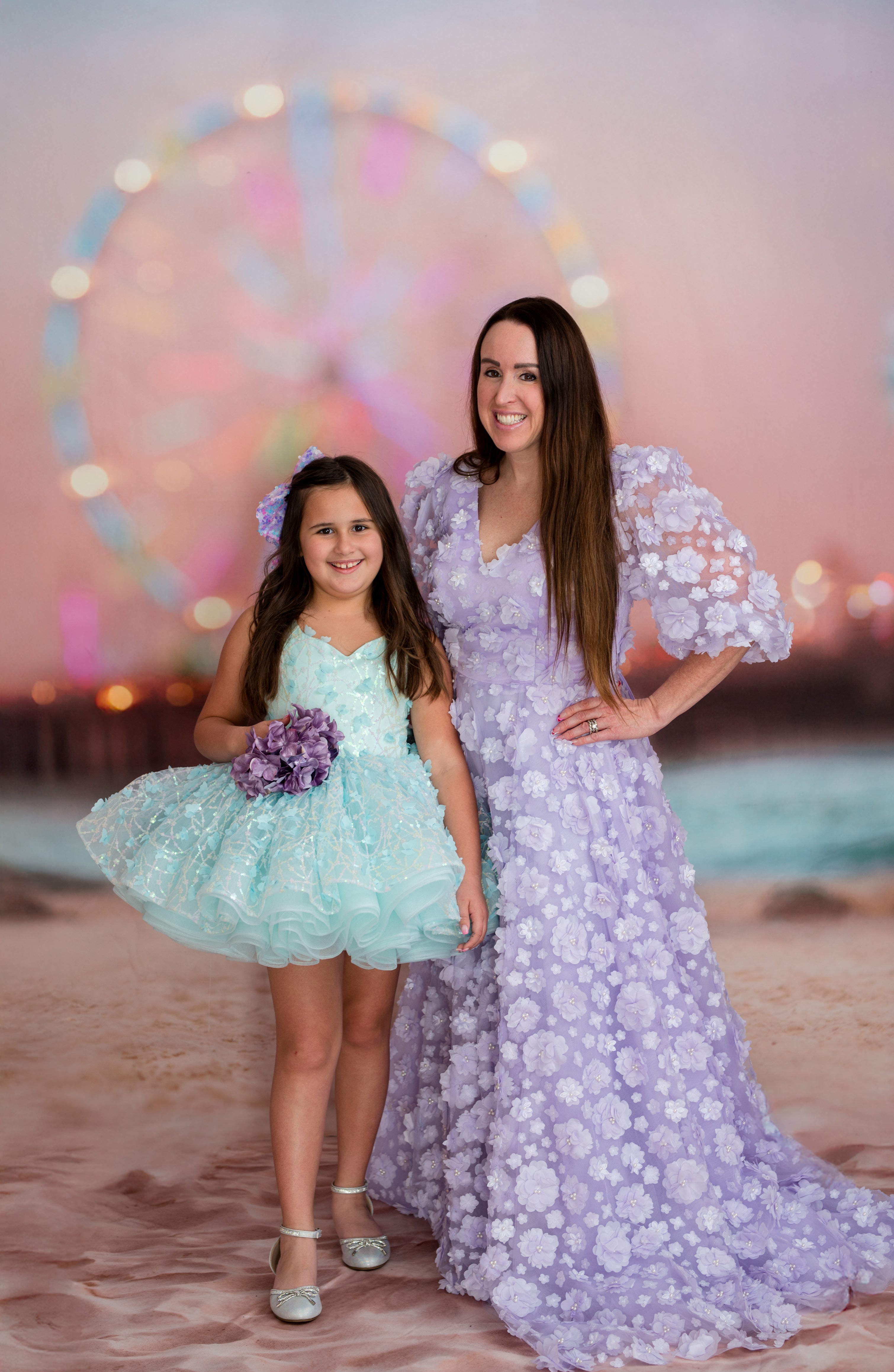 Two women, one in a light blue dress and the other in a purple floral dress, standing in front of a Ferris wheel.