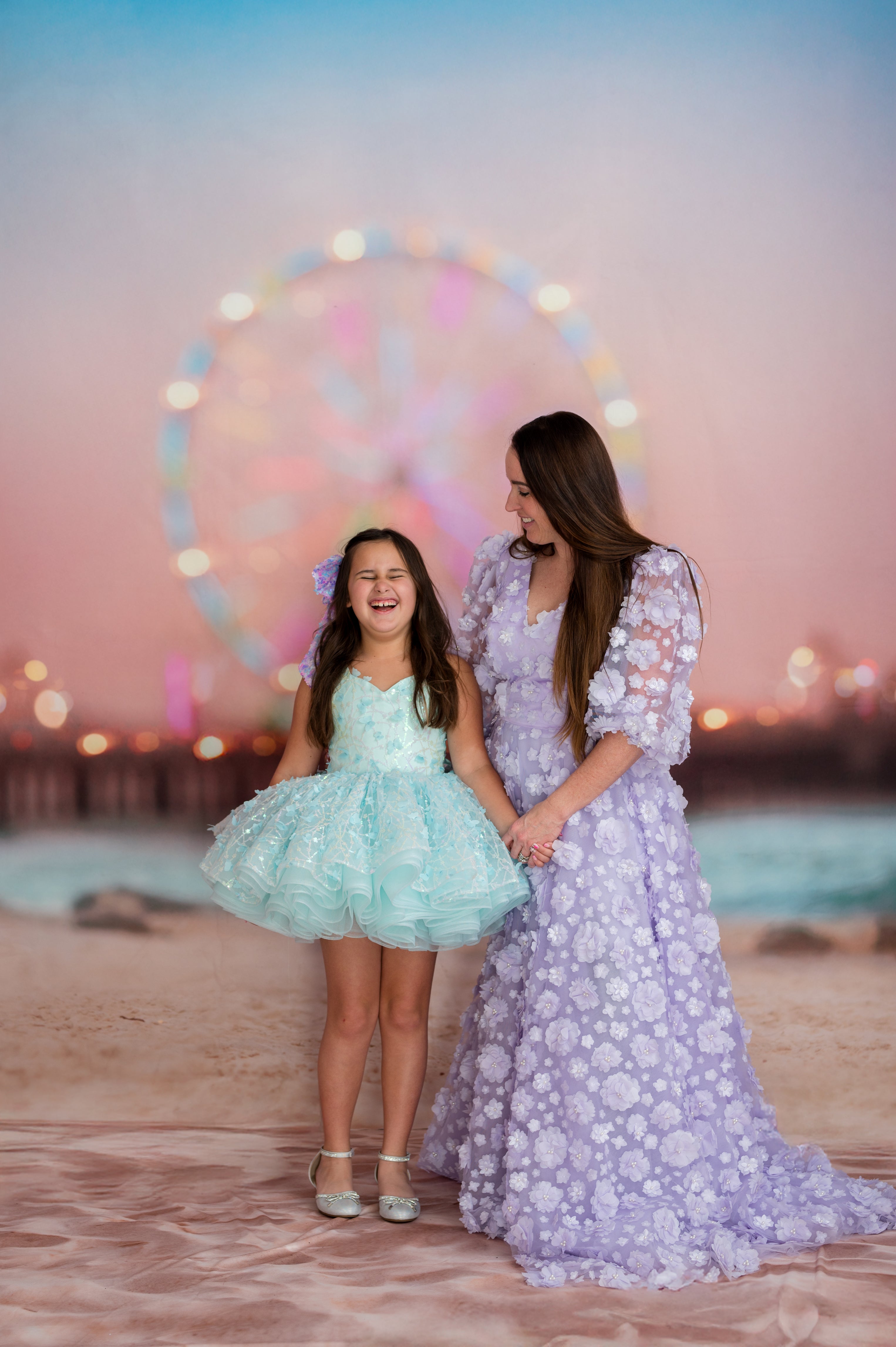 Two women standing on a beach with a Ferris wheel in the background