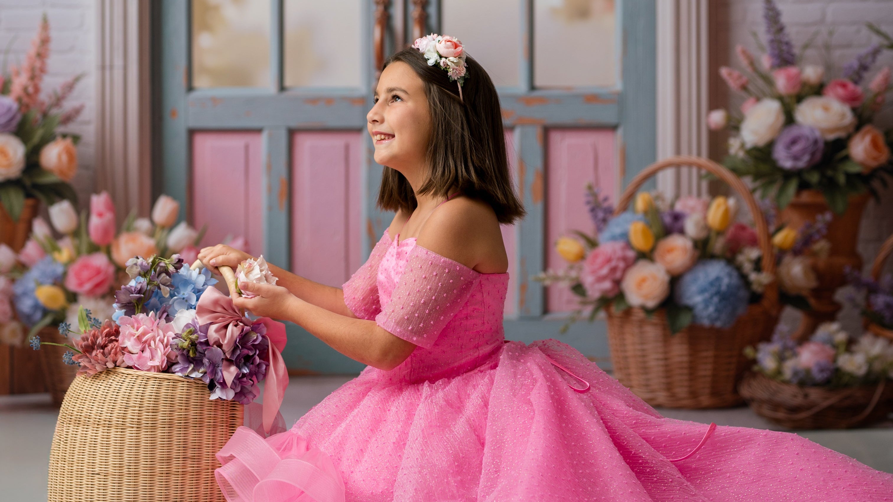 Young girl in a pink dress holding flowers in a decorated room with floral arrangements.