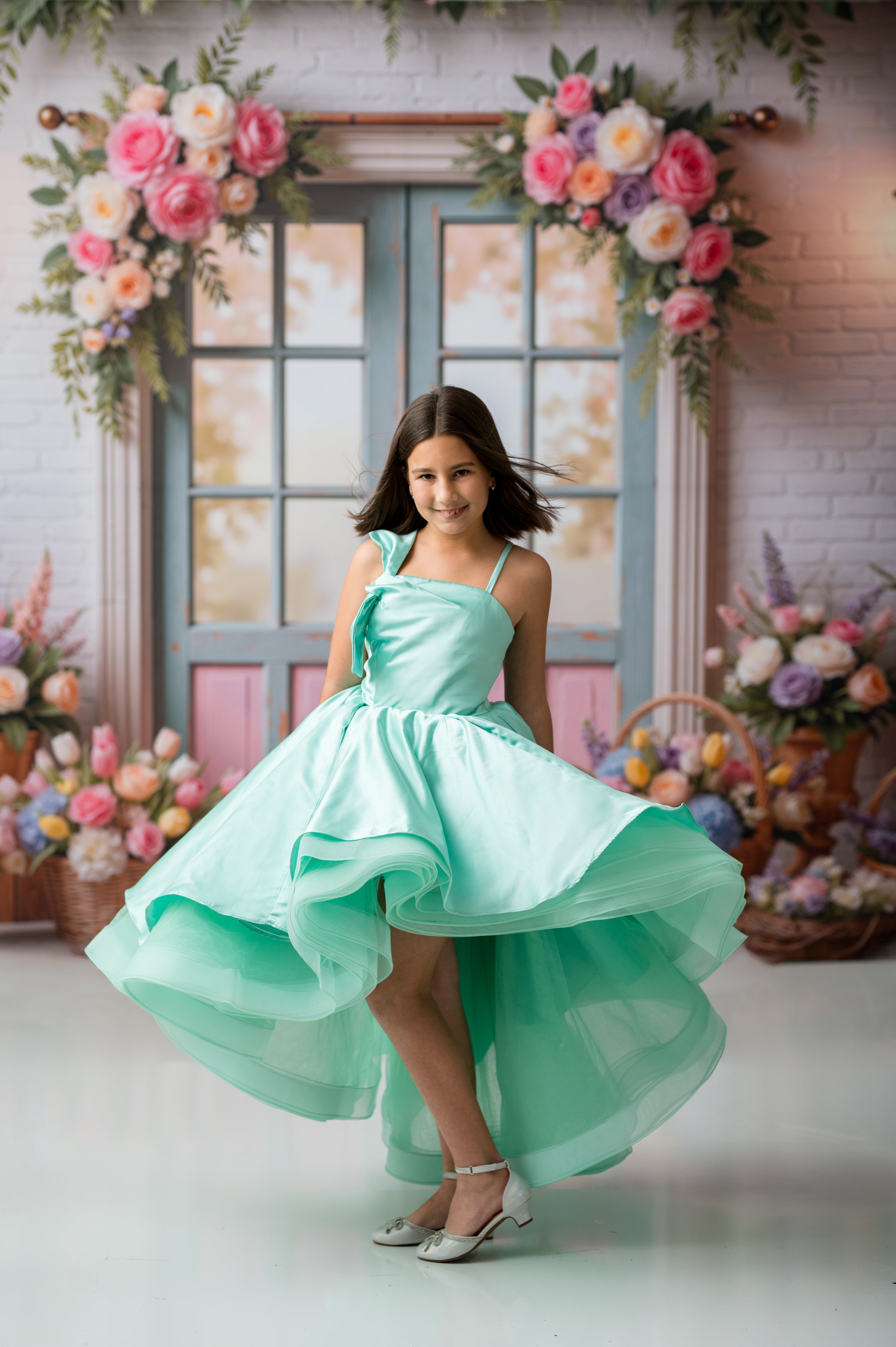 Young girl in a light blue dress standing in front of floral decorations.