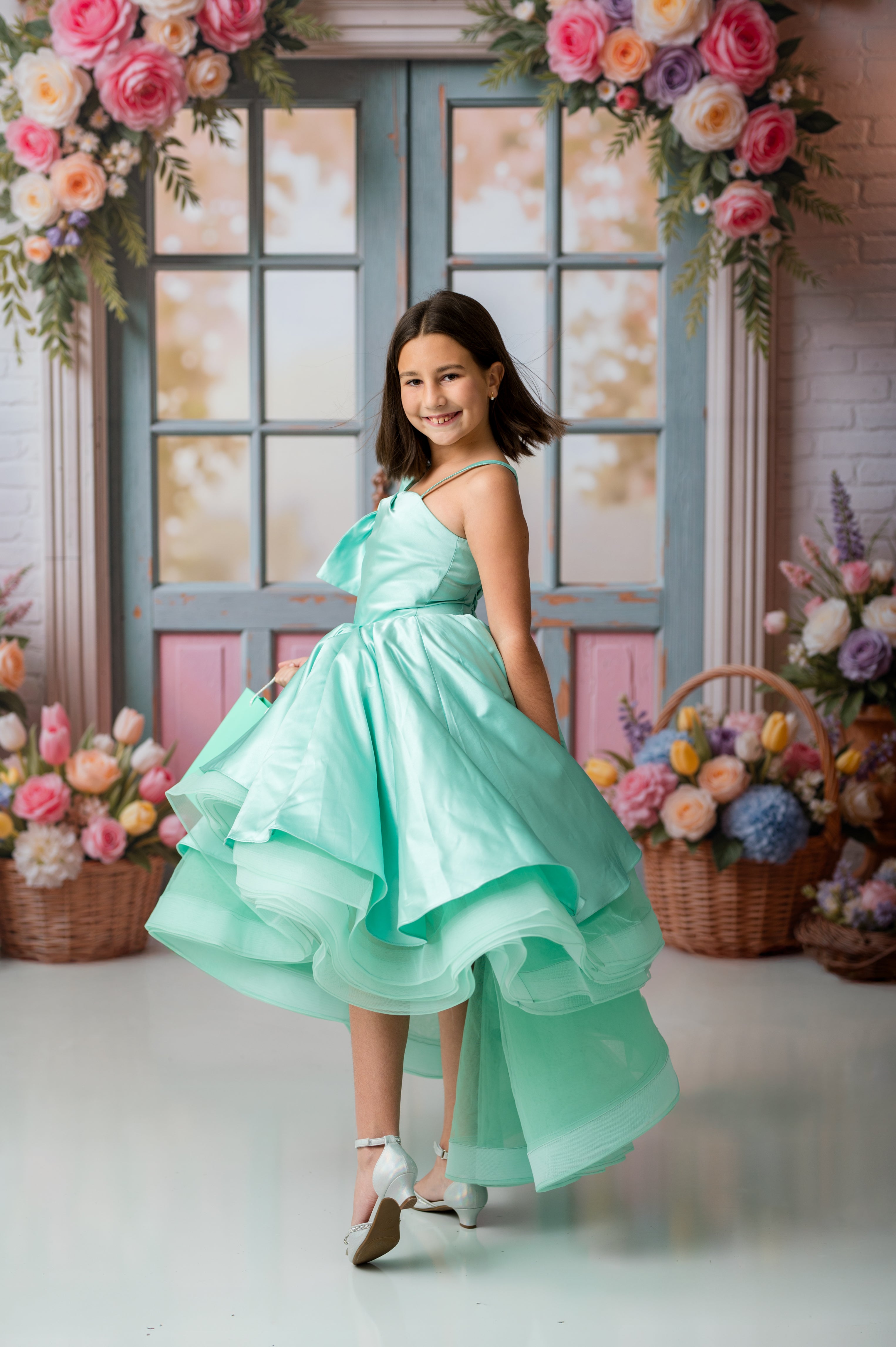 Young girl in a light green dress standing in a decorated room with flowers.