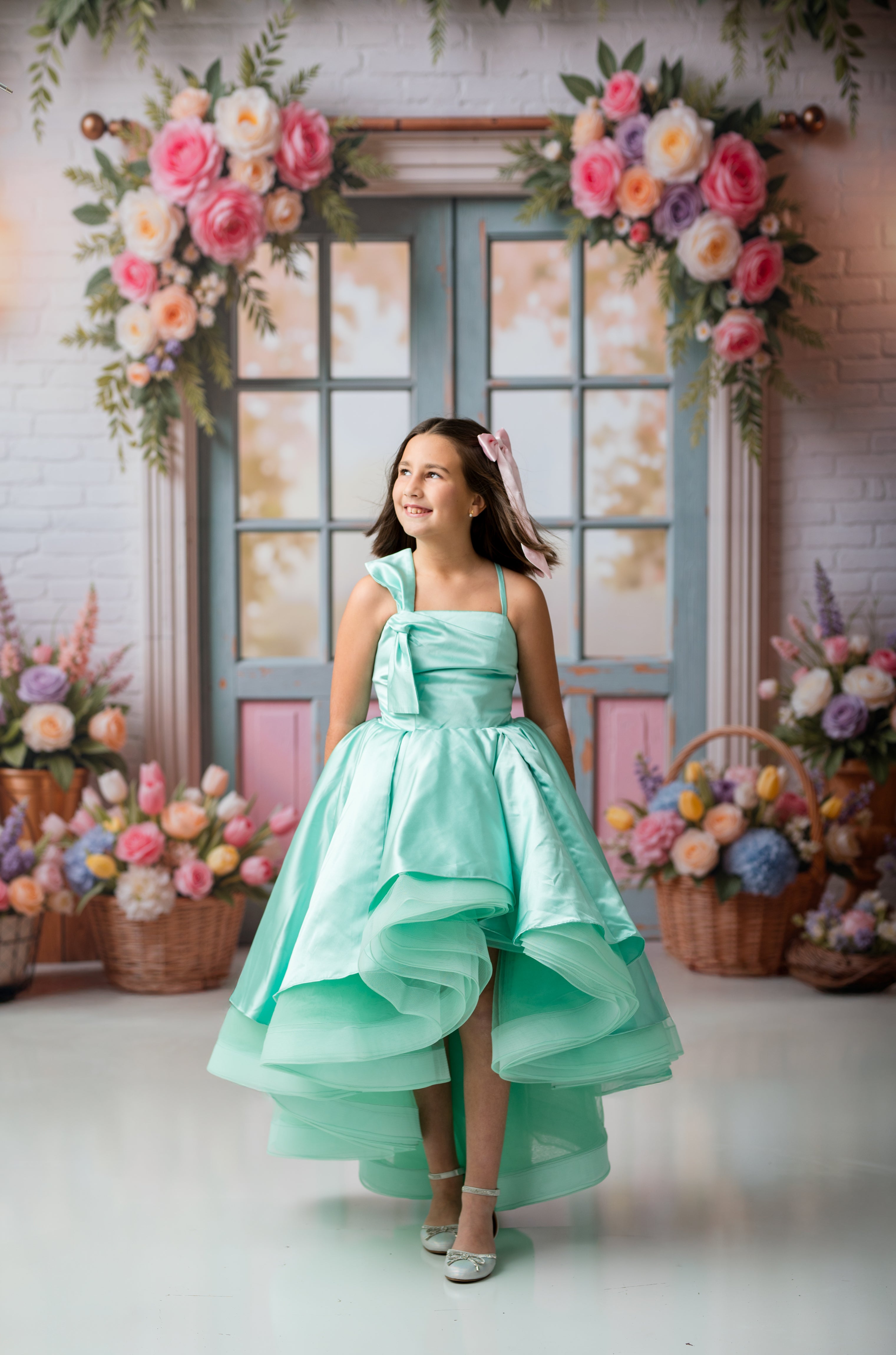 Young girl in a mint green dress standing in front of a floral decorated backdrop.