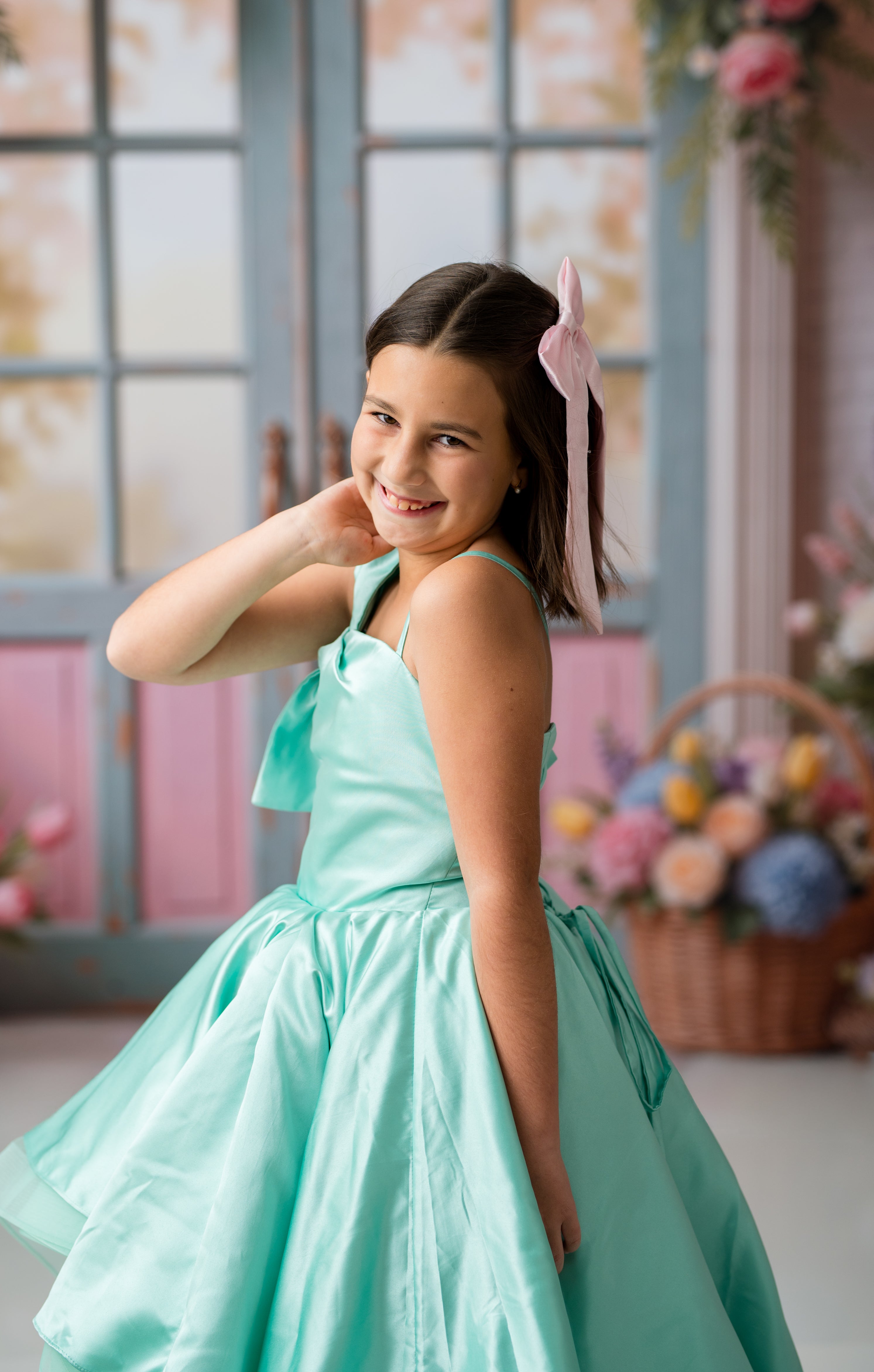 Young girl in a turquoise dress posing in a room with flowers and a pink door.