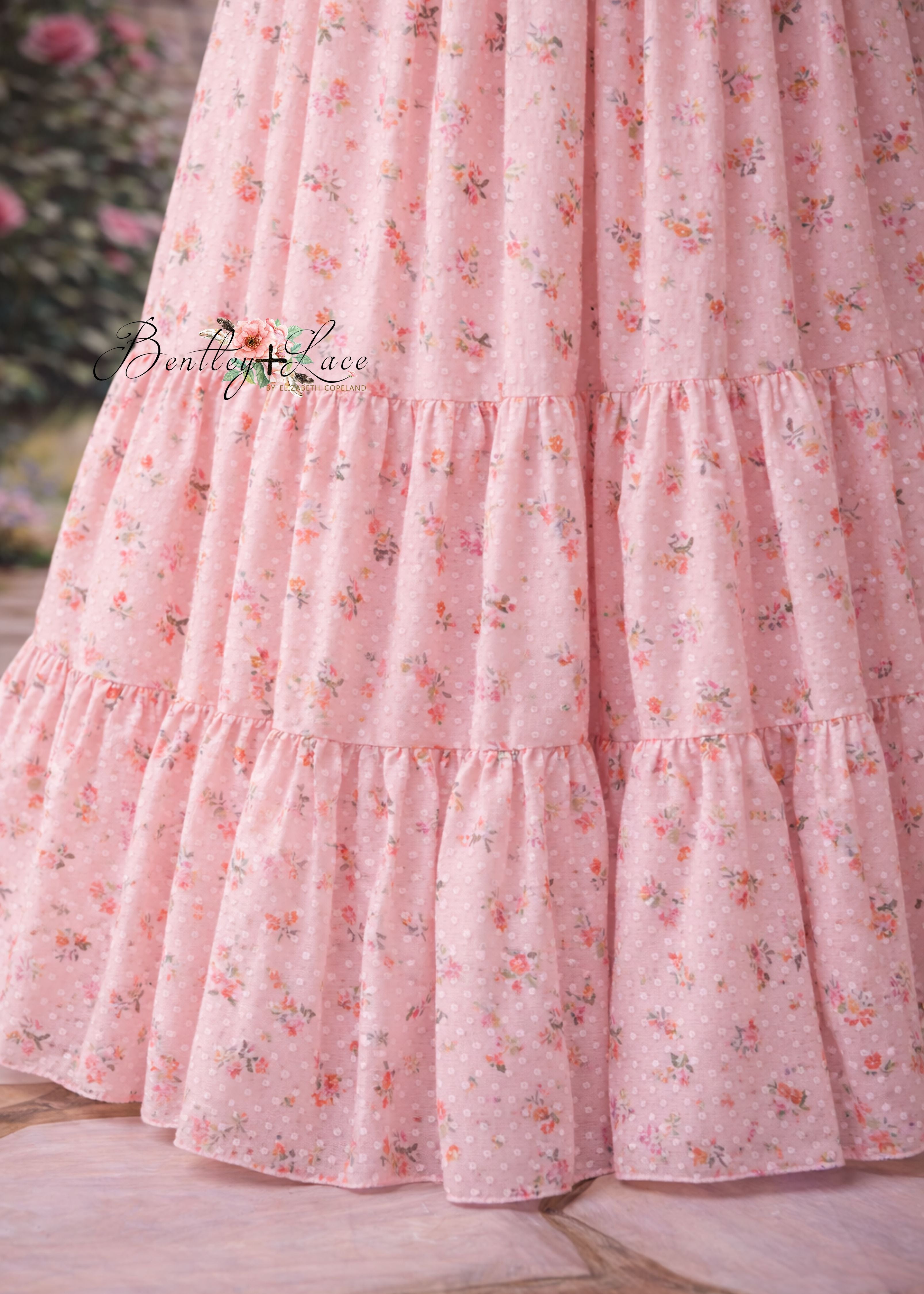 Close-up of a pink floral dress with ruffled layers on a wooden surface.