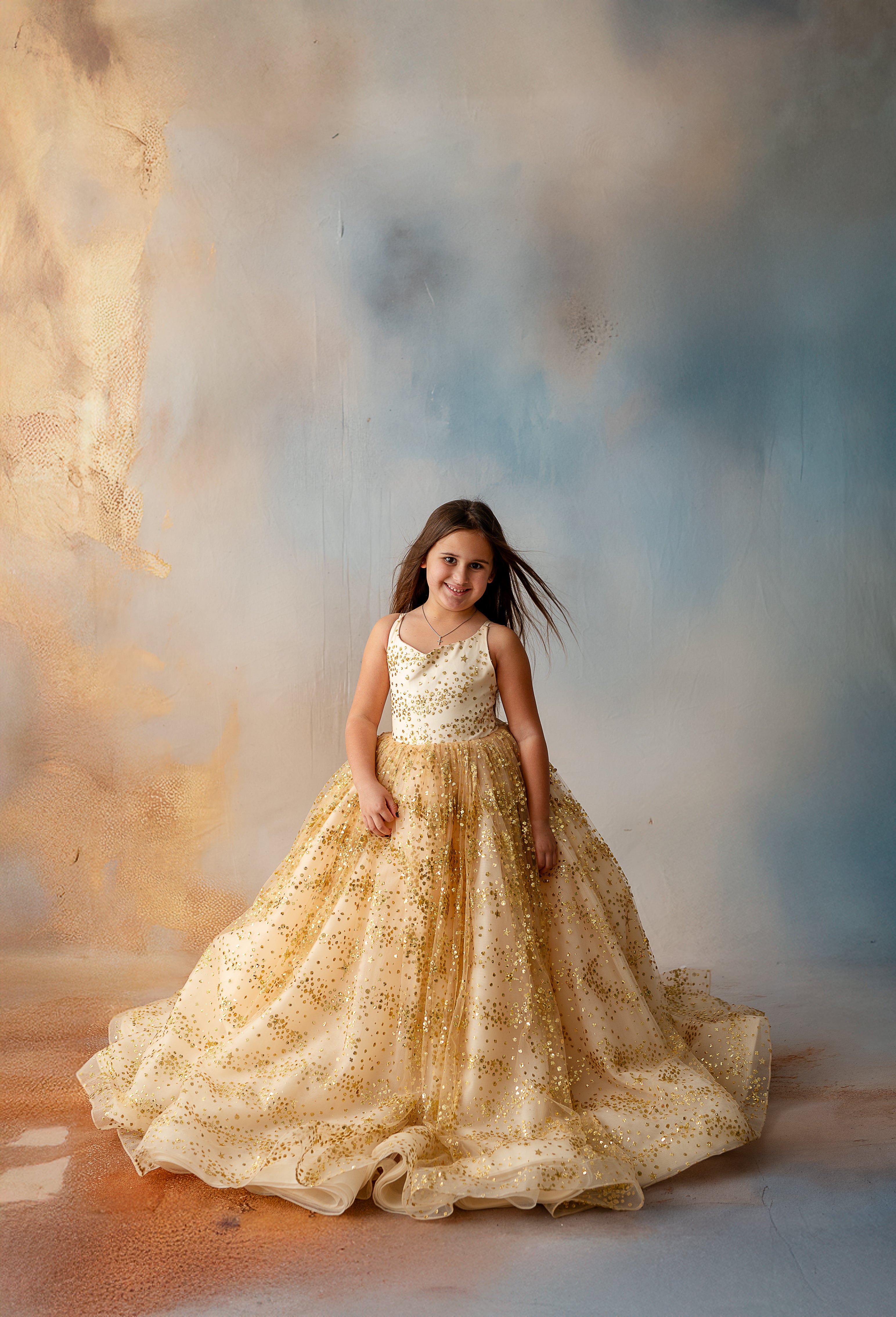 Child posing in floor-length gold star gown under studio lights