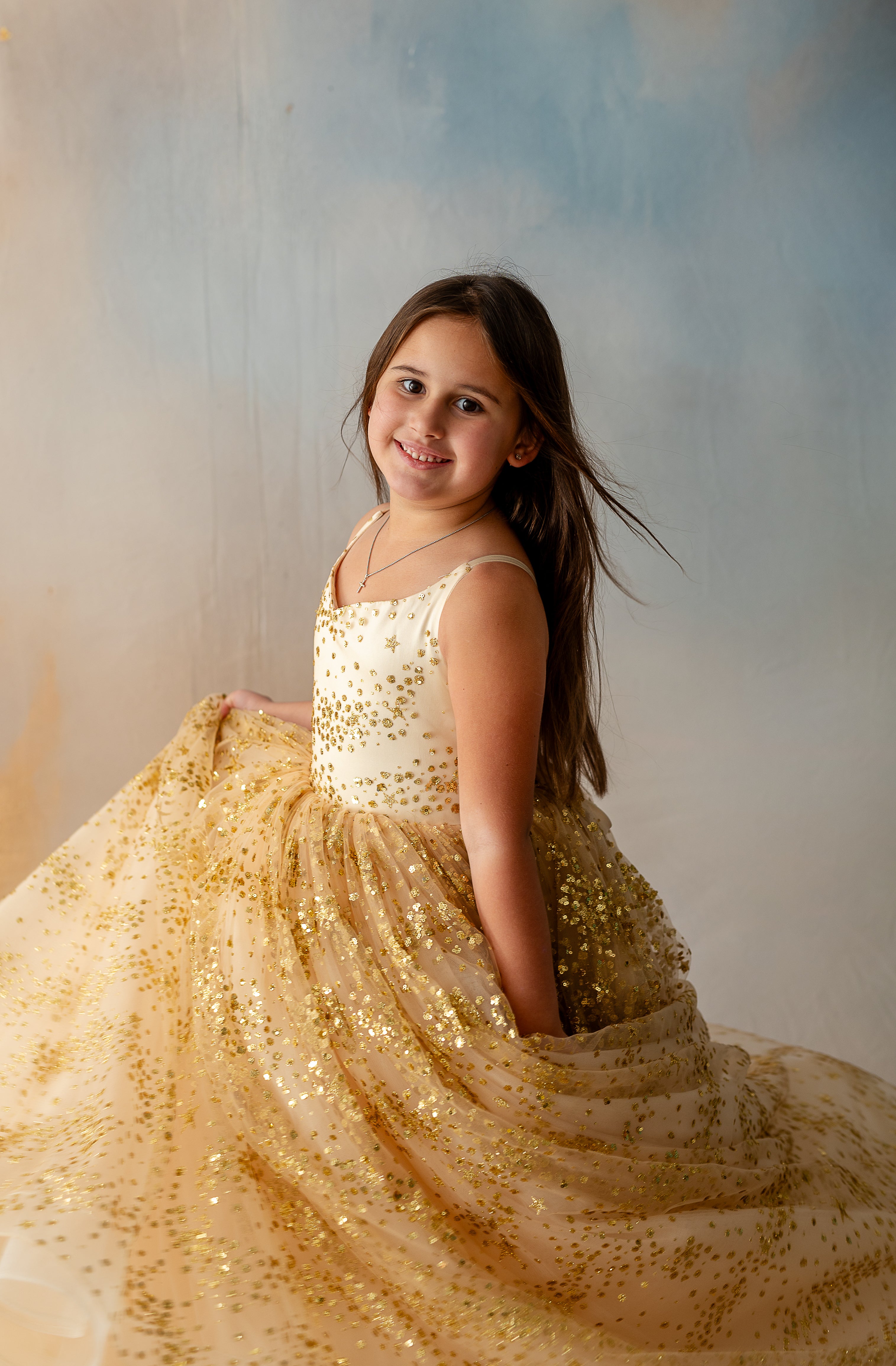 Young model standing in soft light wearing gold glitter gown