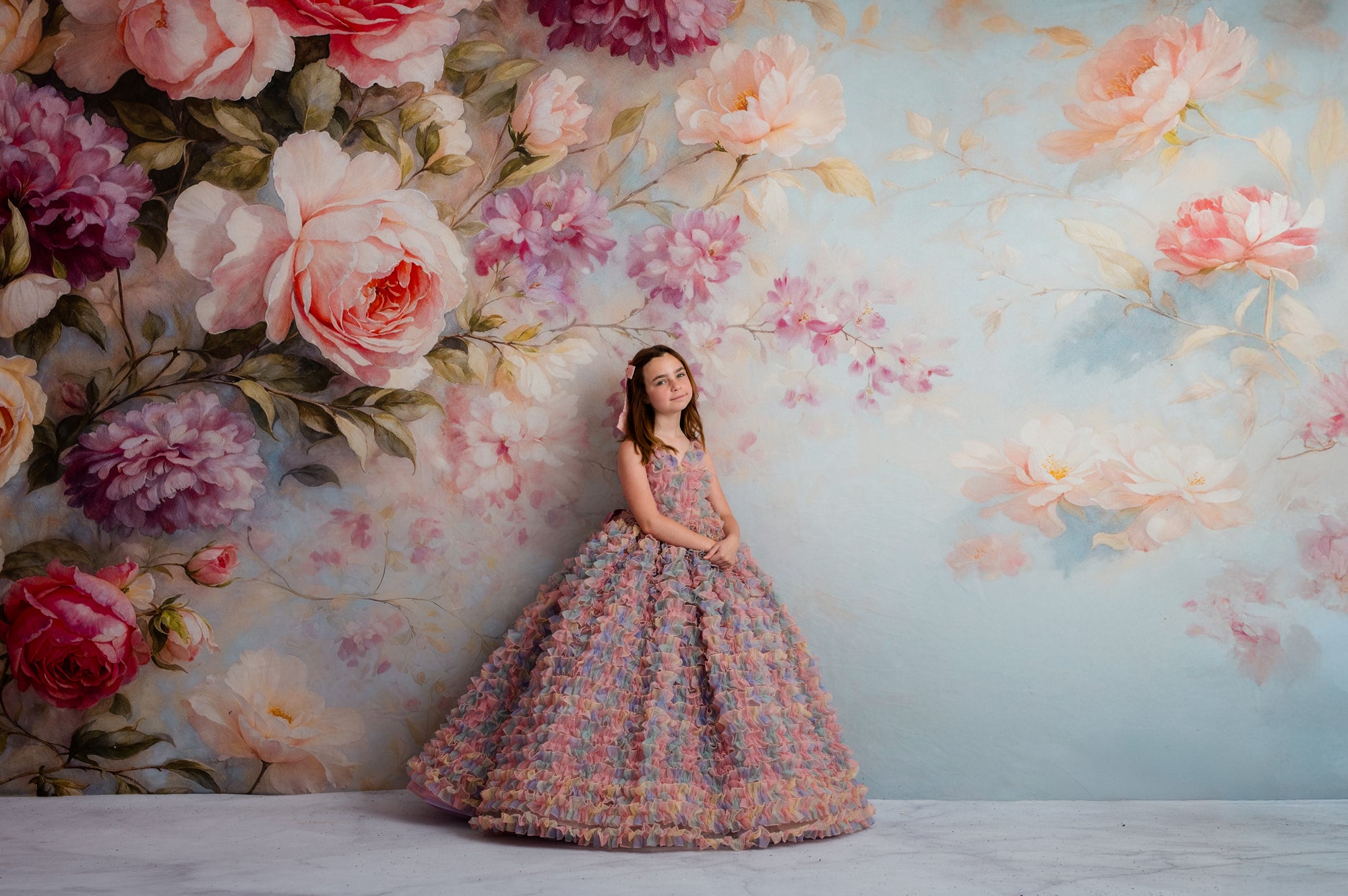 Young girl in a floral dress standing against a floral wall mural.