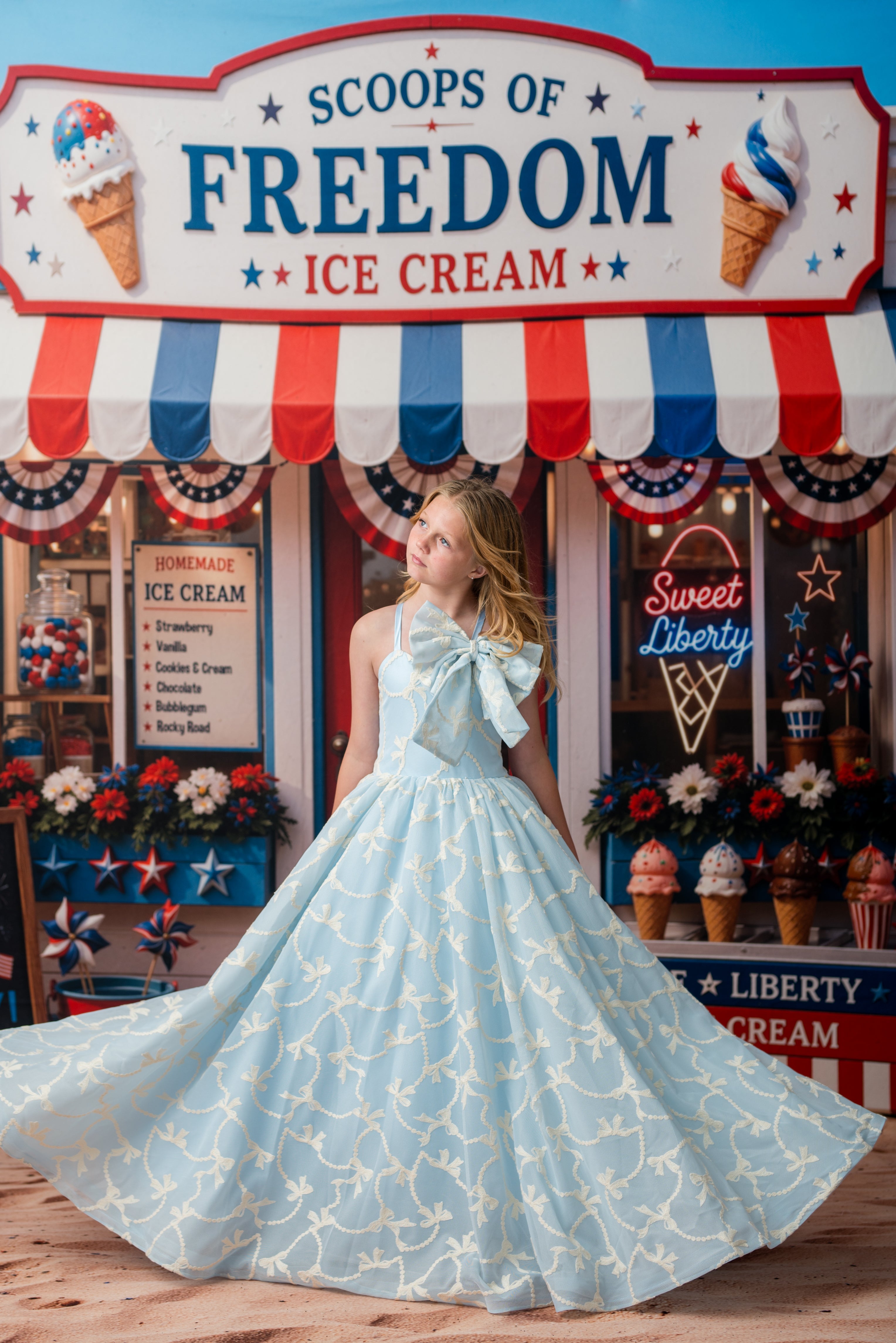 Woman in a light blue dress with a large bow standing in front of 'Scoops of Freedom Ice Cream' sign.