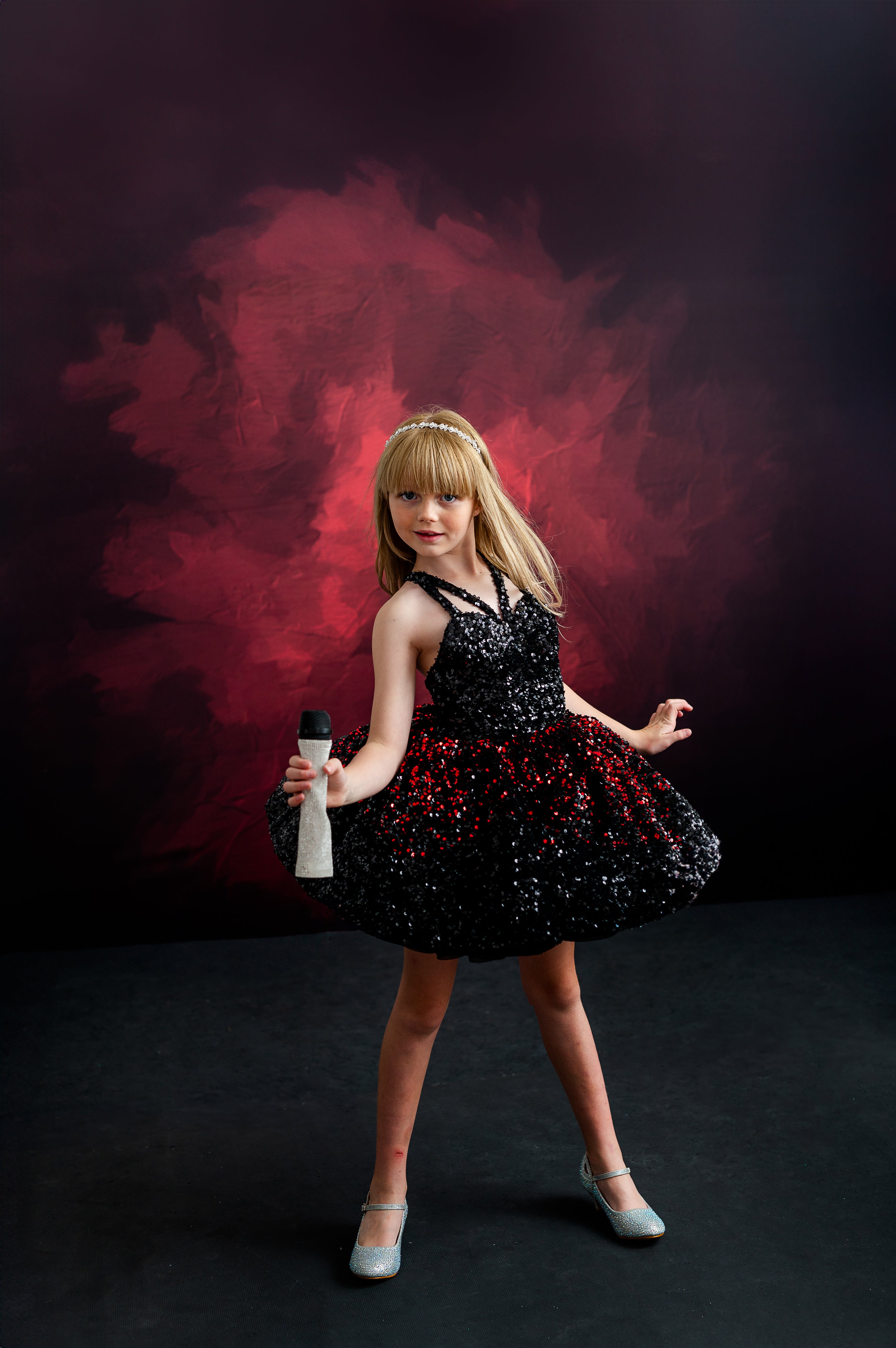 Blonde child in a glittering gown, twirling dramatically in a red and black dress reminiscent of Taylor Swift's iconic style.