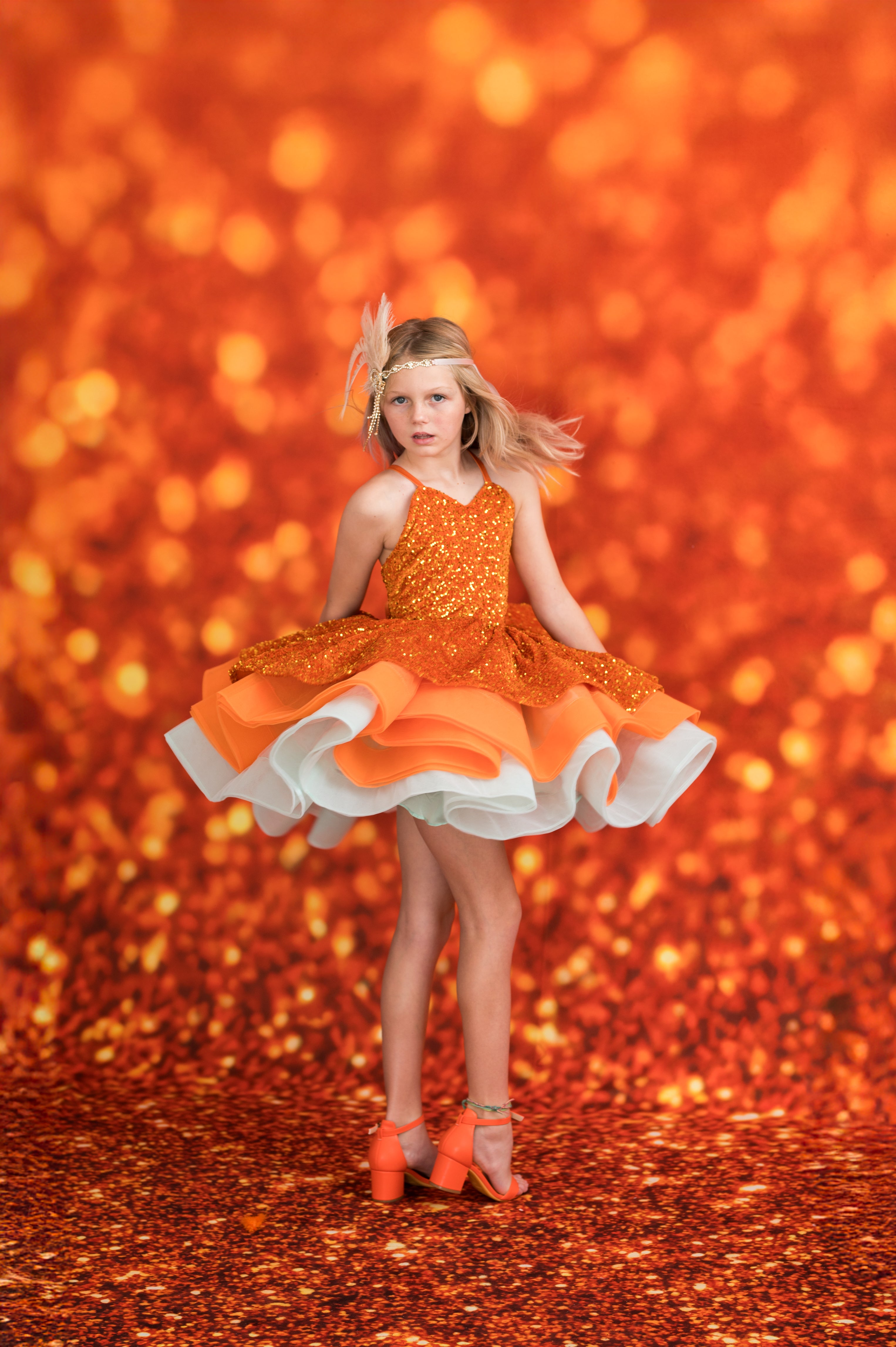 Young girl in an orange dress with a white skirt against a glittery orange background