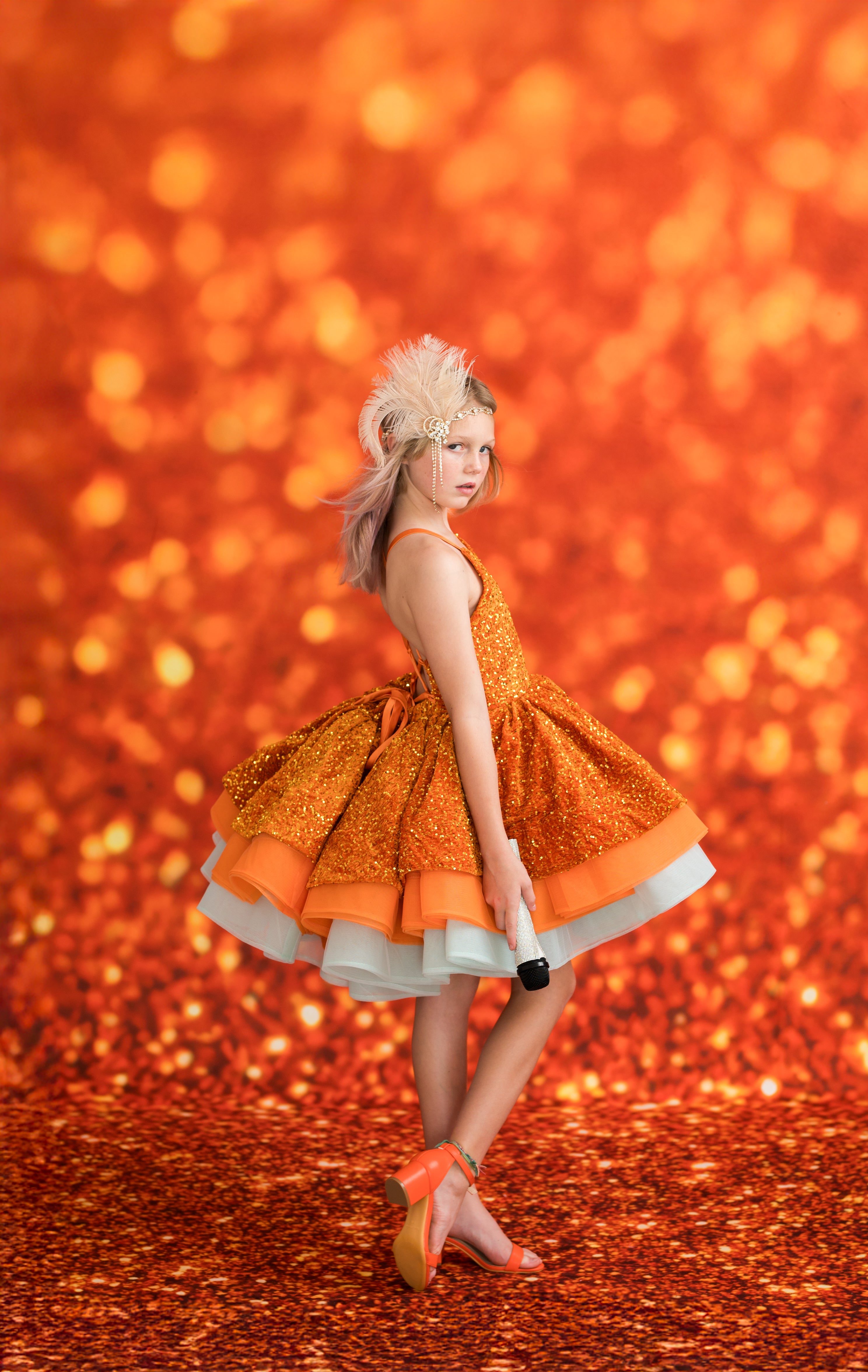 Woman in an orange dress with a white skirt against a glittery orange background