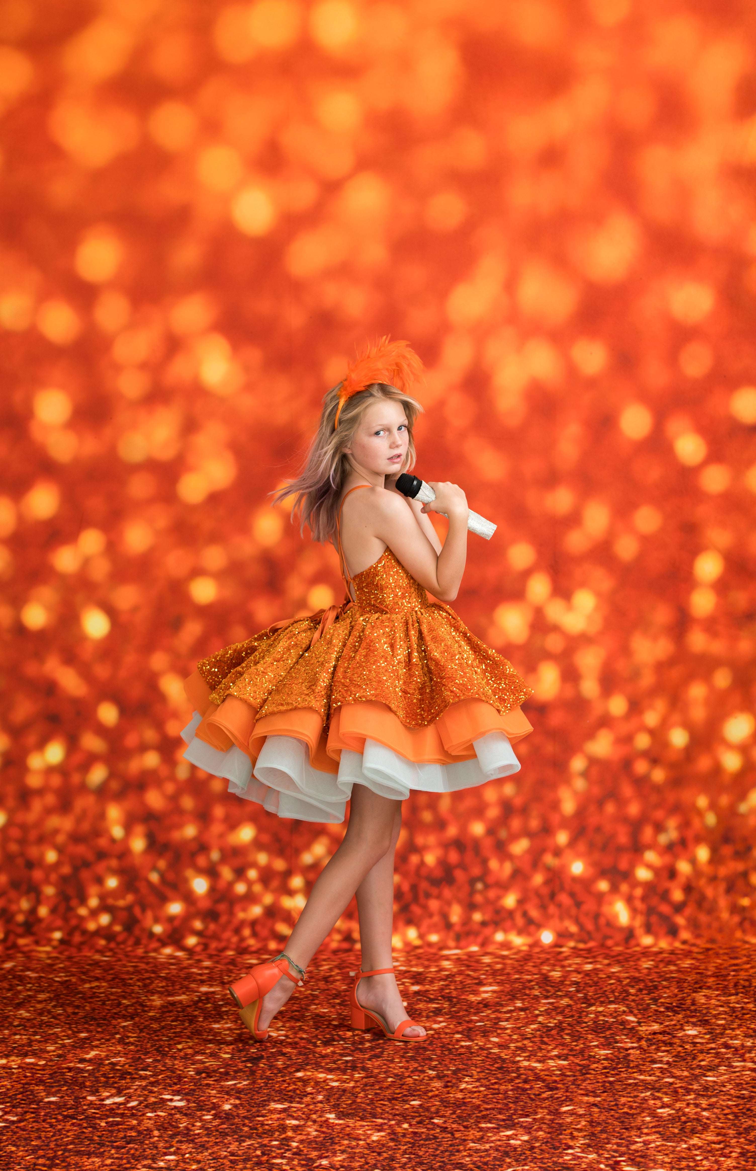 Girl in an orange dress posing against a glittery orange background- Taylor Swift Inspired - LIFE OF A SHOWGIRL