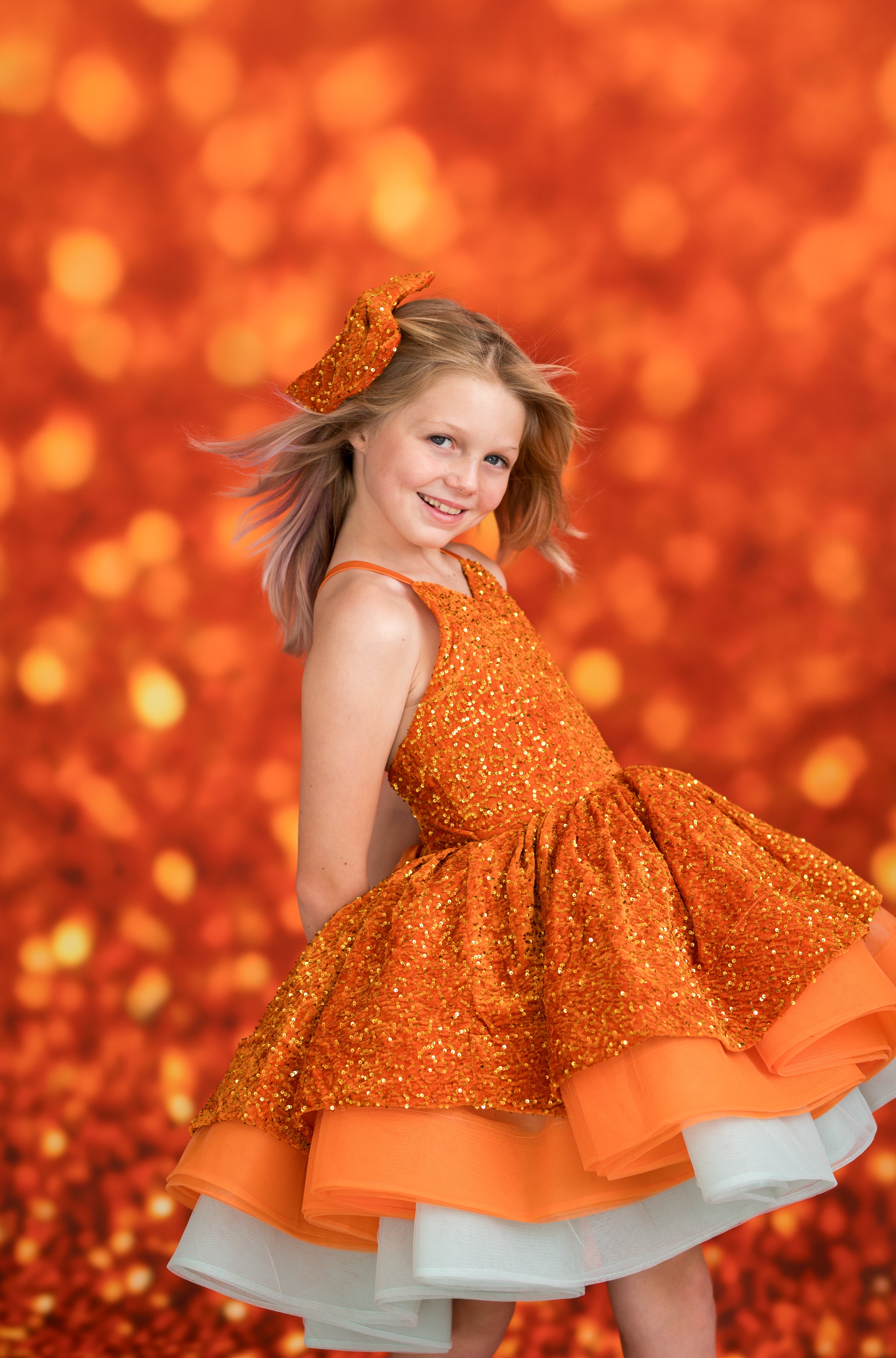Young girl in an orange dress with a sparkling texture against a warm, blurred background