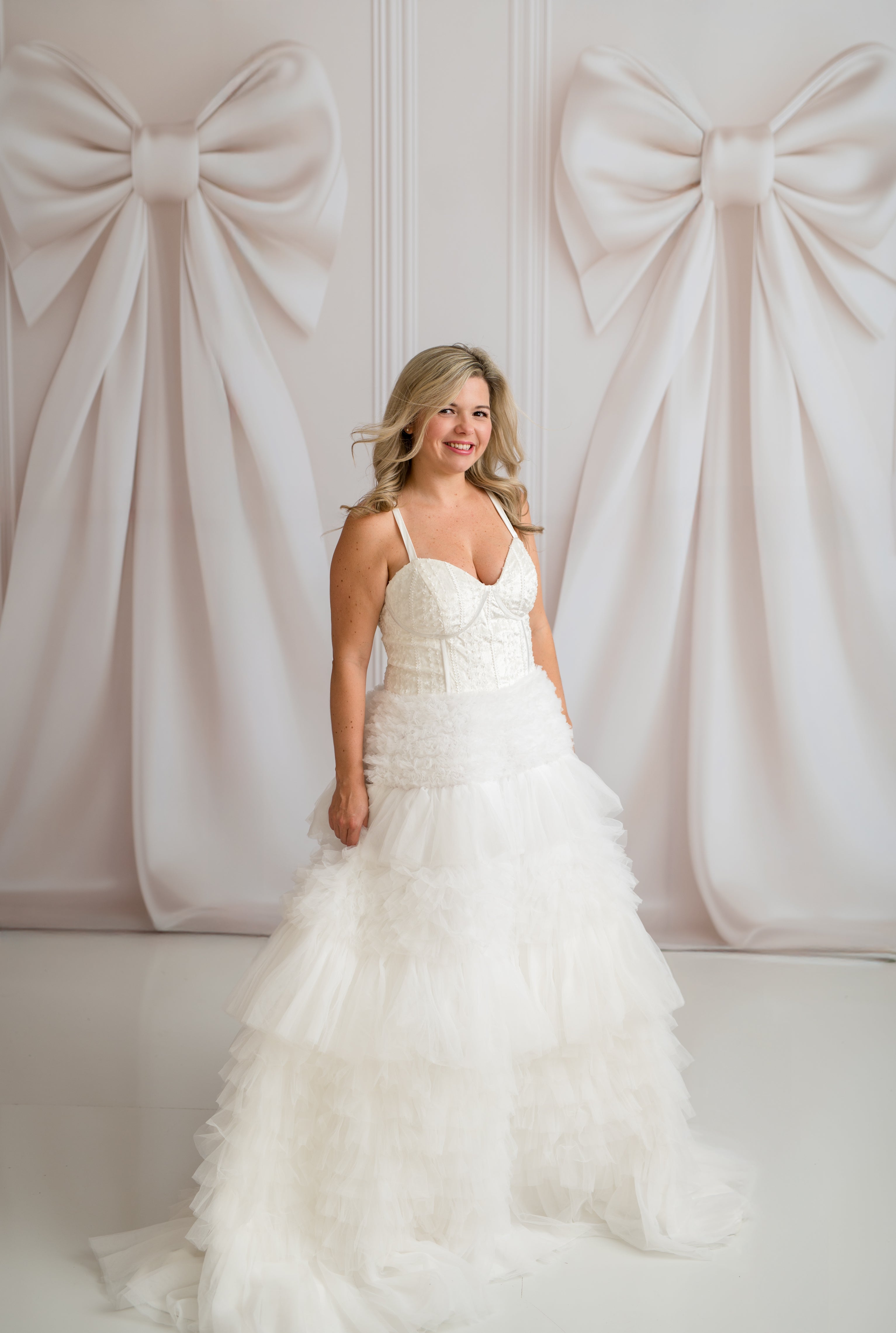 Woman in a white wedding dress standing in front of a decorative wall with large bows.