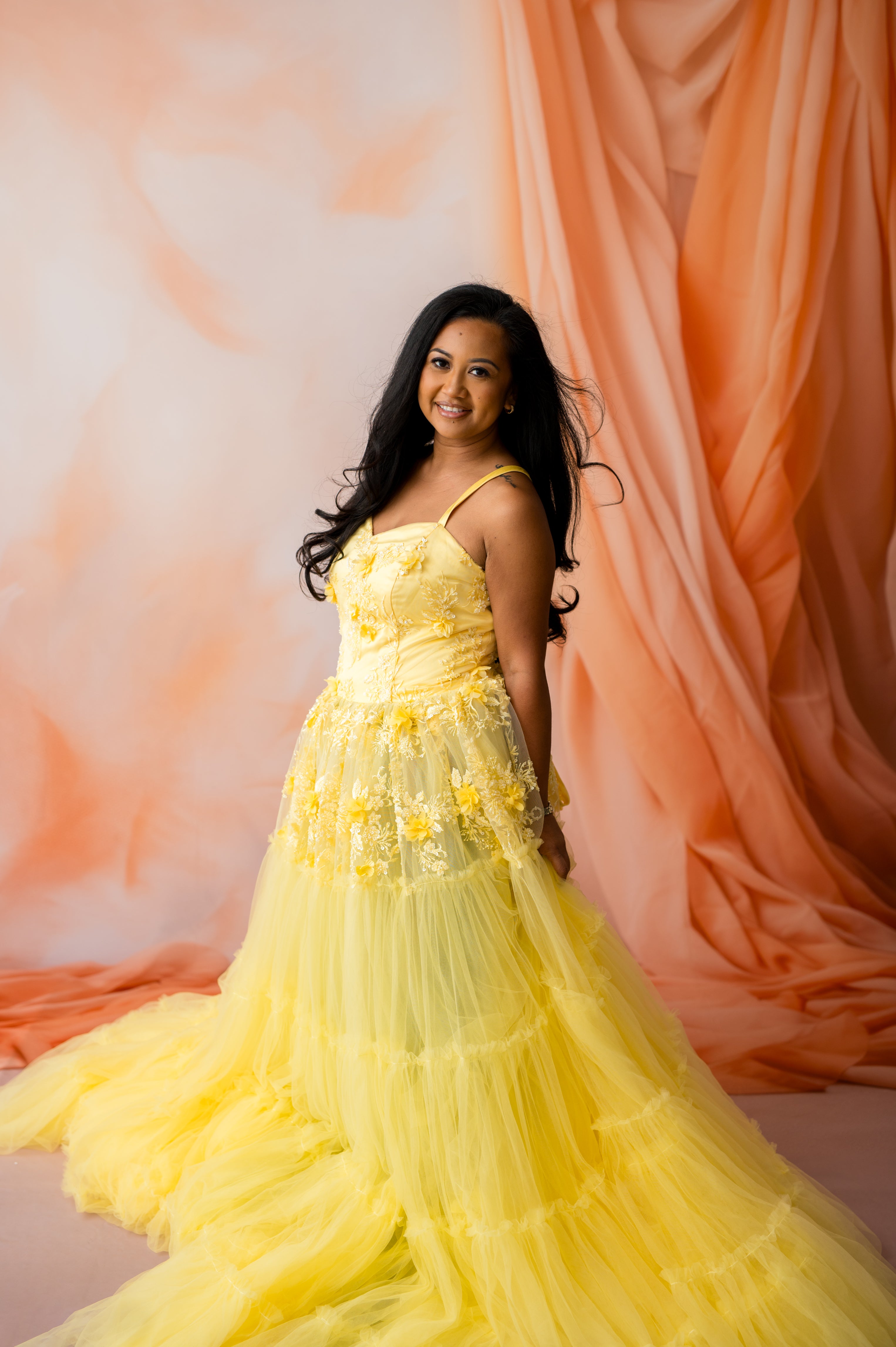 Woman in a yellow dress standing against an orange curtain backdrop