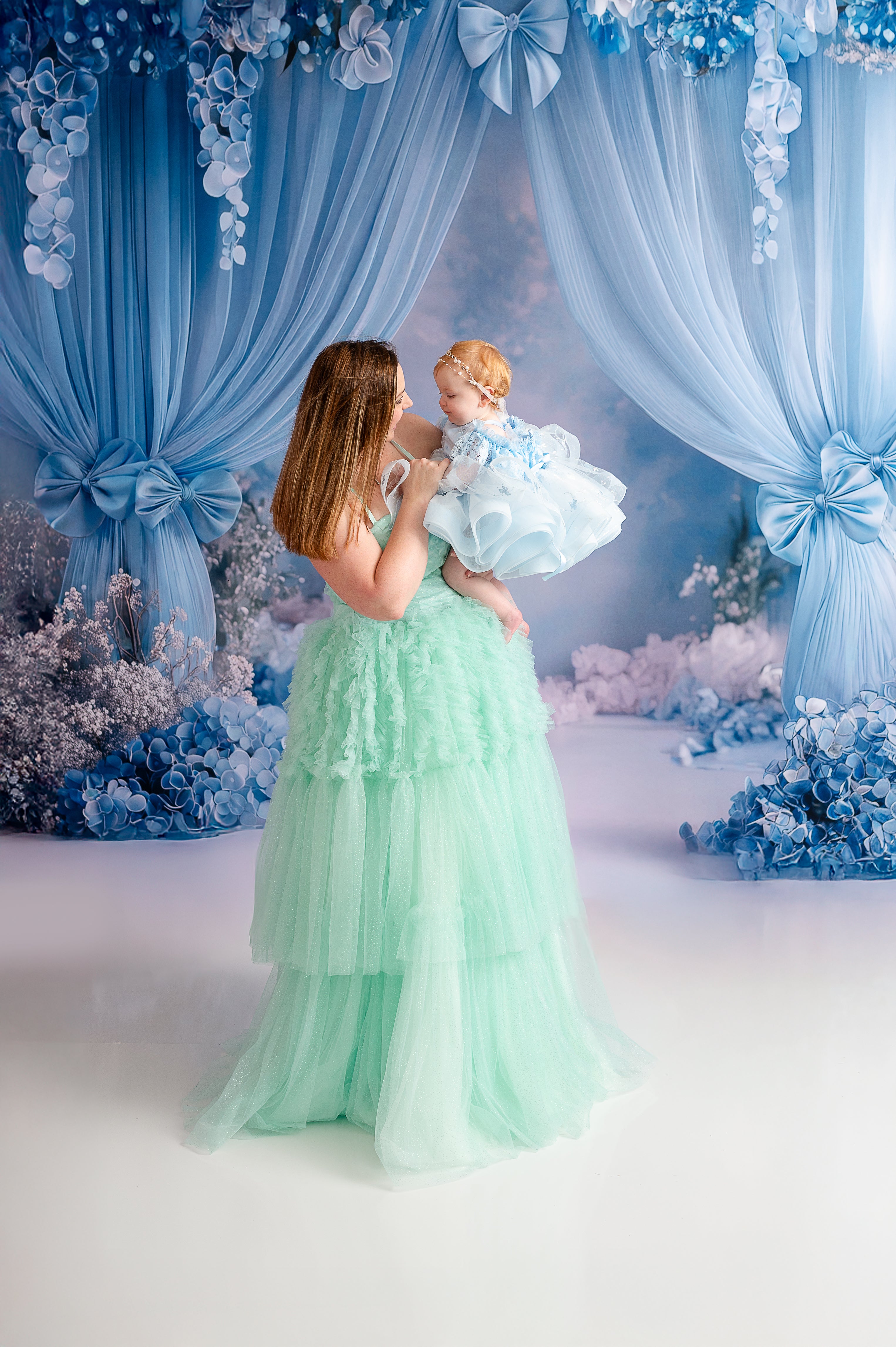 A mother and daughter pose in couture gowns with delicate tulle details, creating a fairytale-like scene.