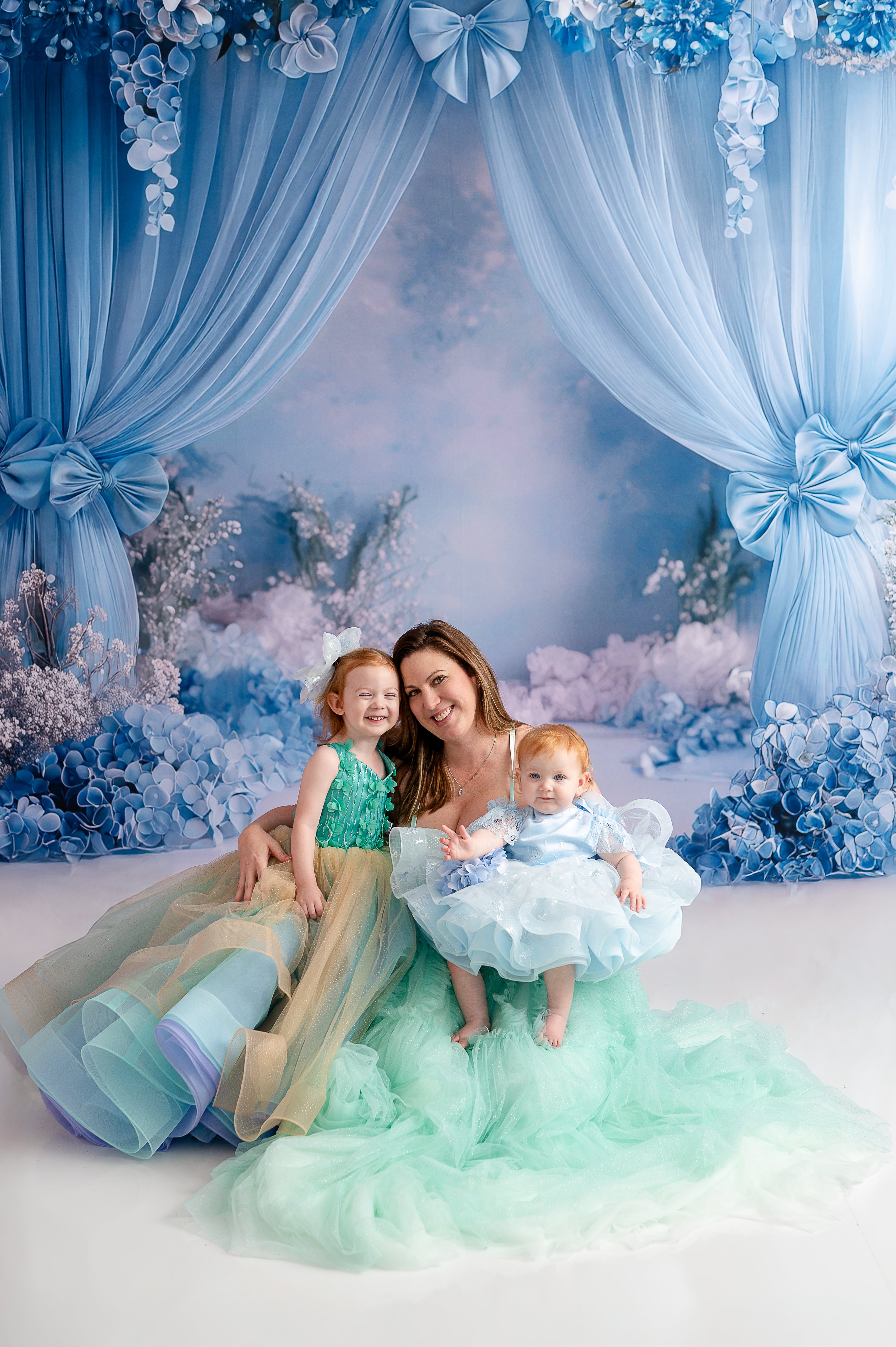 A woman and her daughter in matching gowns pose for an elegant studio photography session.