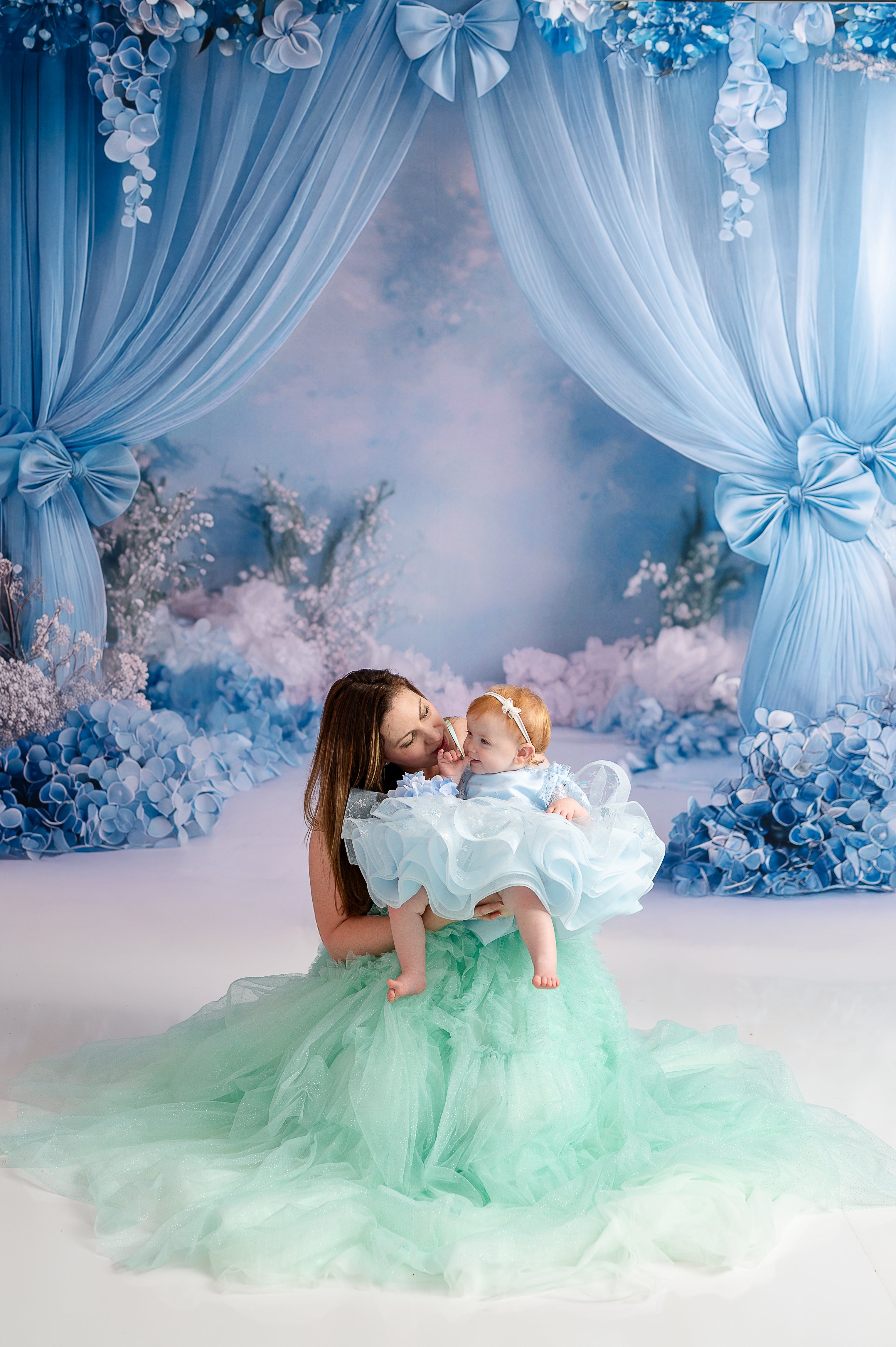 A mother and daughter, dressed in elegant pastel tulle dresses, share a joyful connection in a whimsical setting.