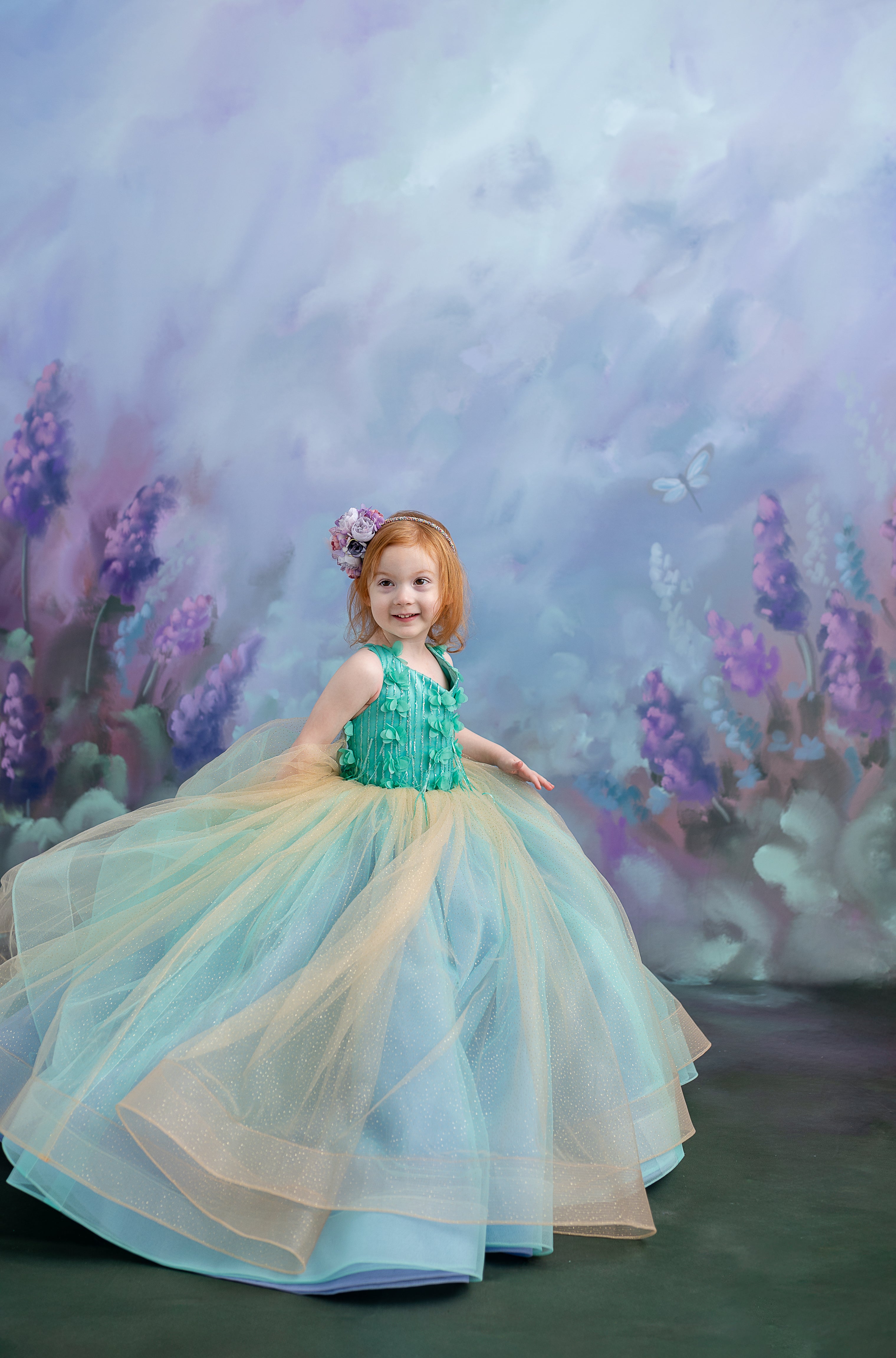 Toddler princess moment – a child sitting gracefully in the Evelyn gown, framed by dreamy blue drapery.