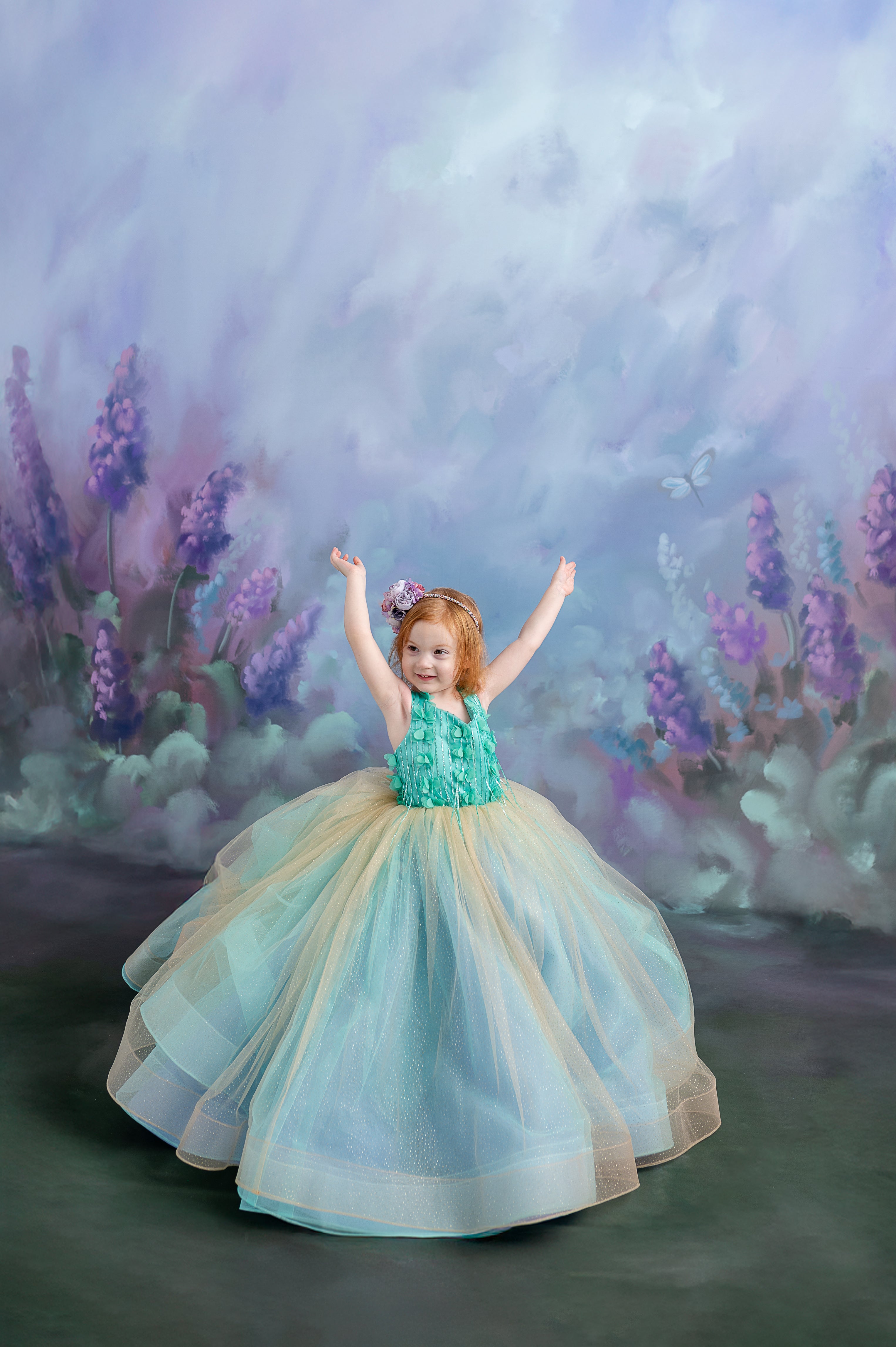 Side profile of a toddler in the gown, holding a matching floral accessory in a soft-lit studio.
