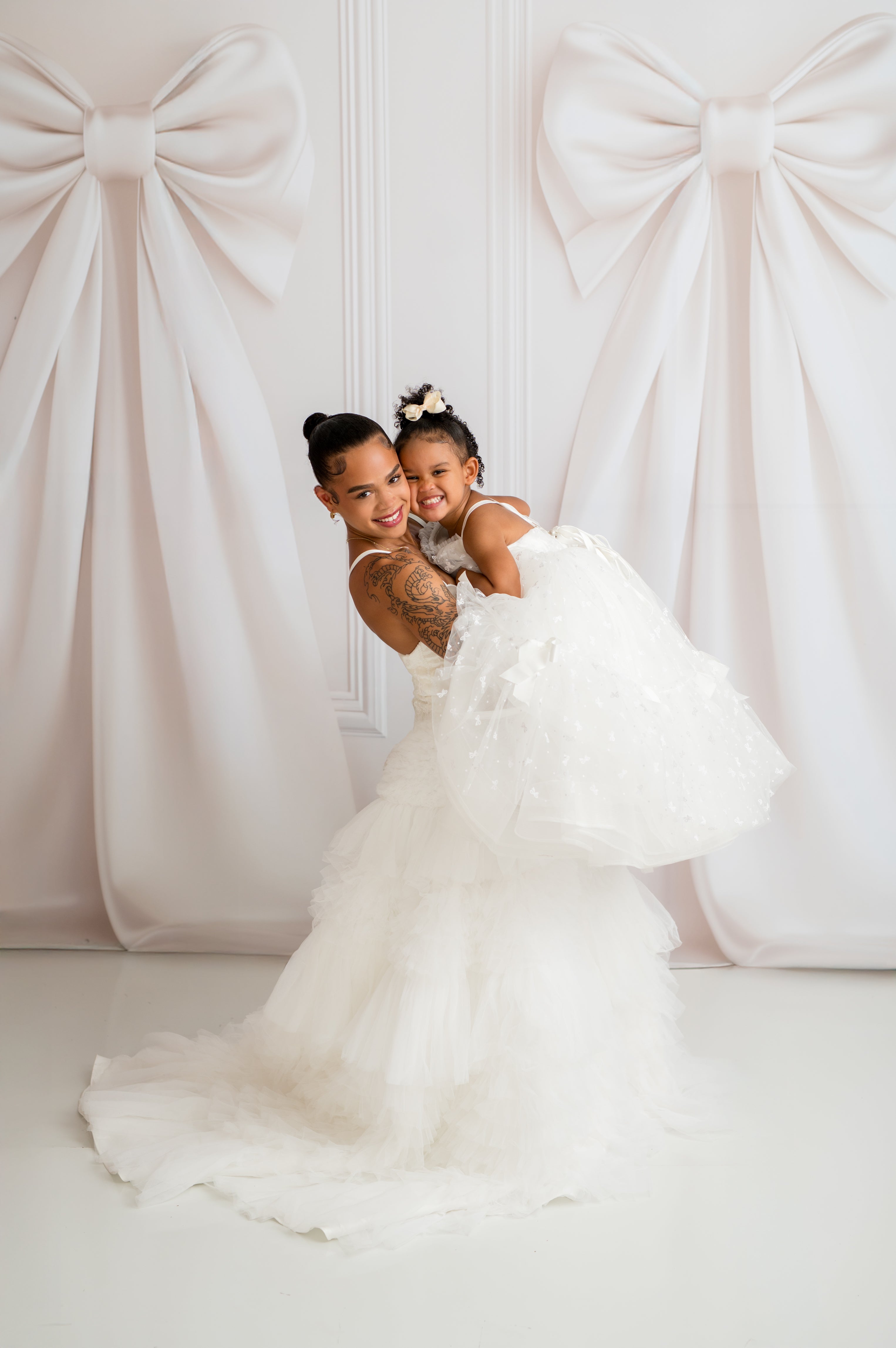 Two women in white dresses posing against a decorative white curtain.