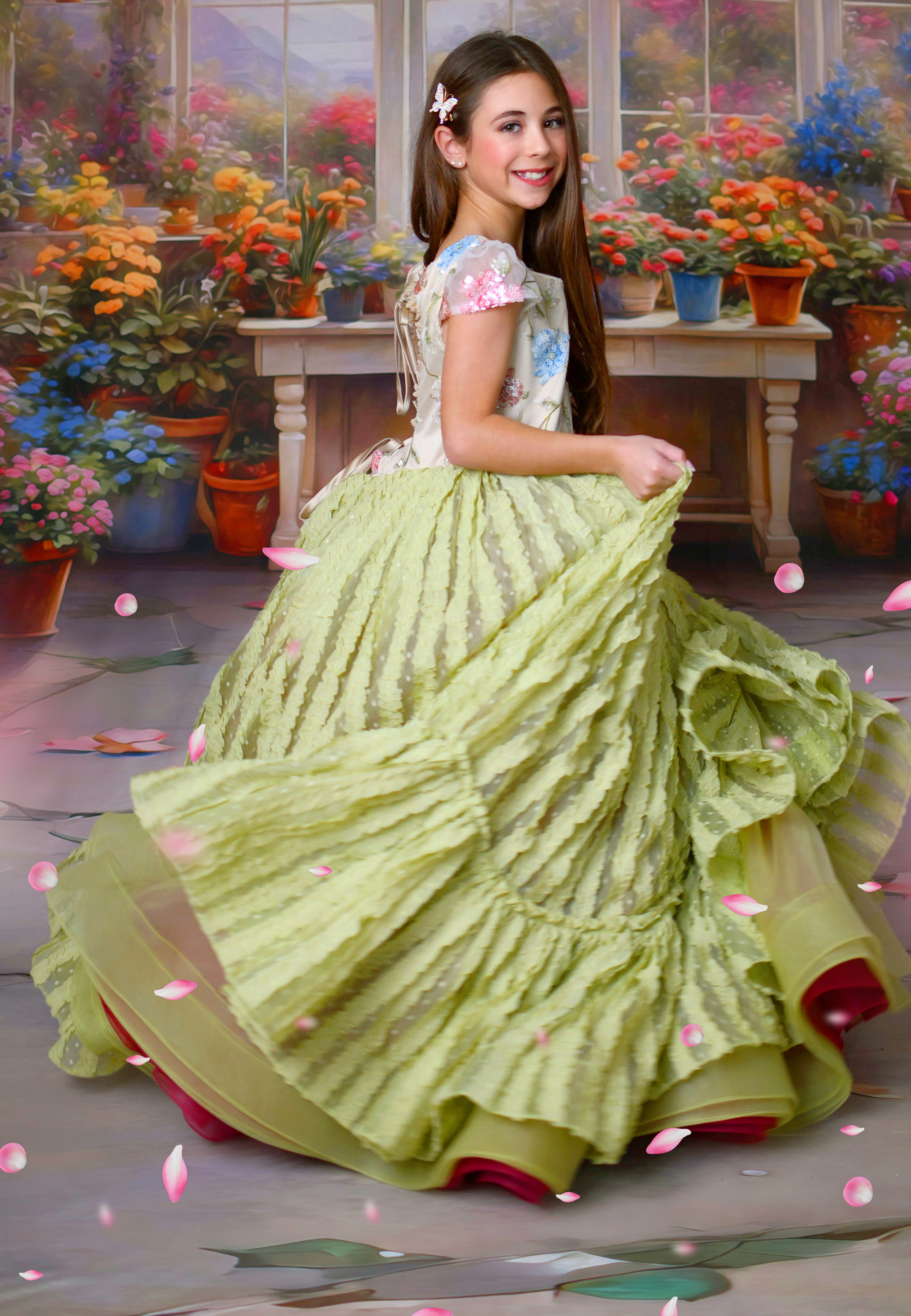Girl in a flowing green floral gown posing in front of a greenhouse-themed floral backdrop.