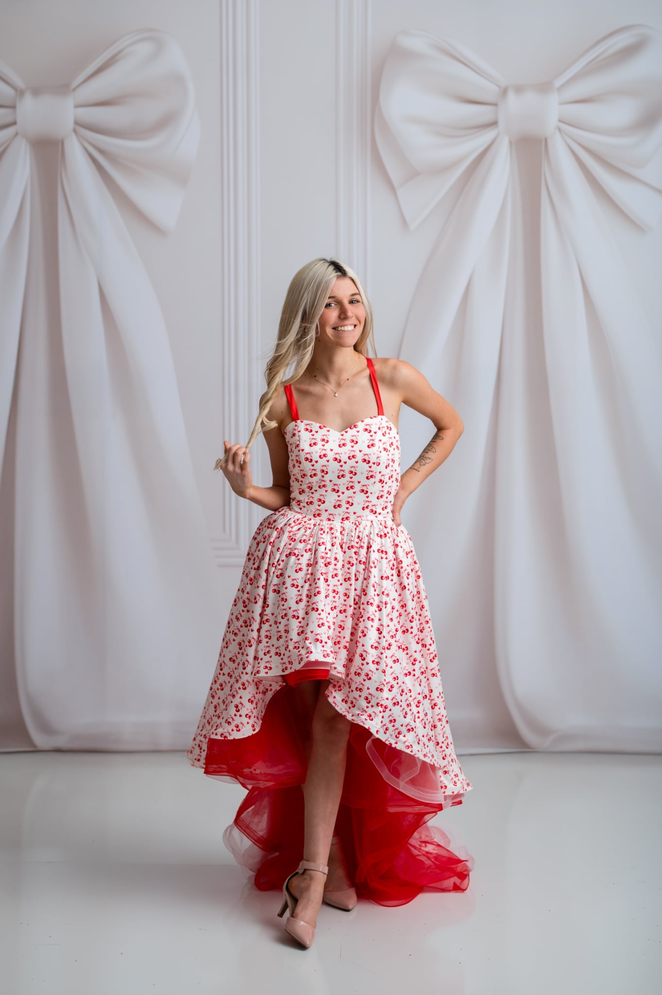 Woman in a red and white floral dress standing against a white background with large bows.