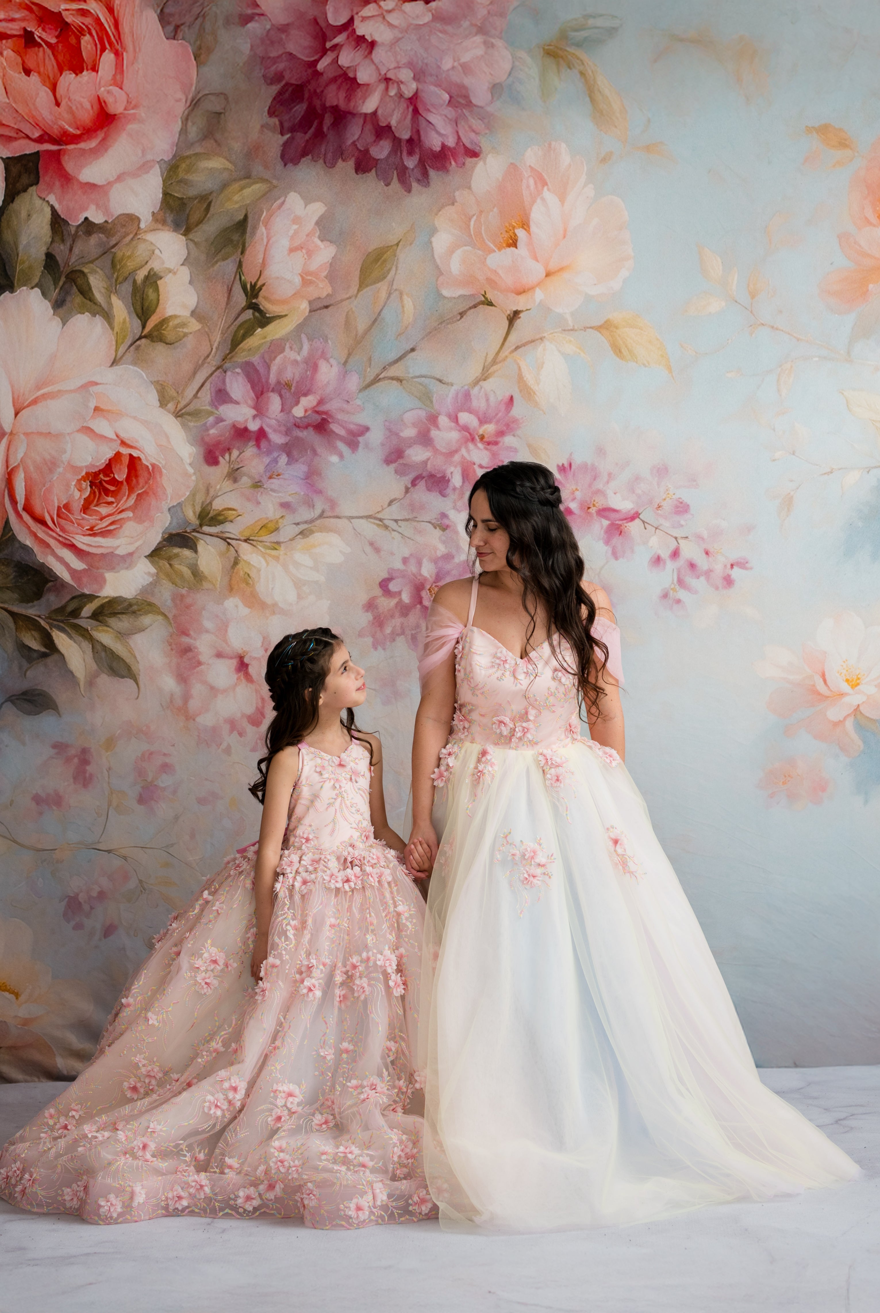 Two women in floral dresses standing against a floral backdrop
