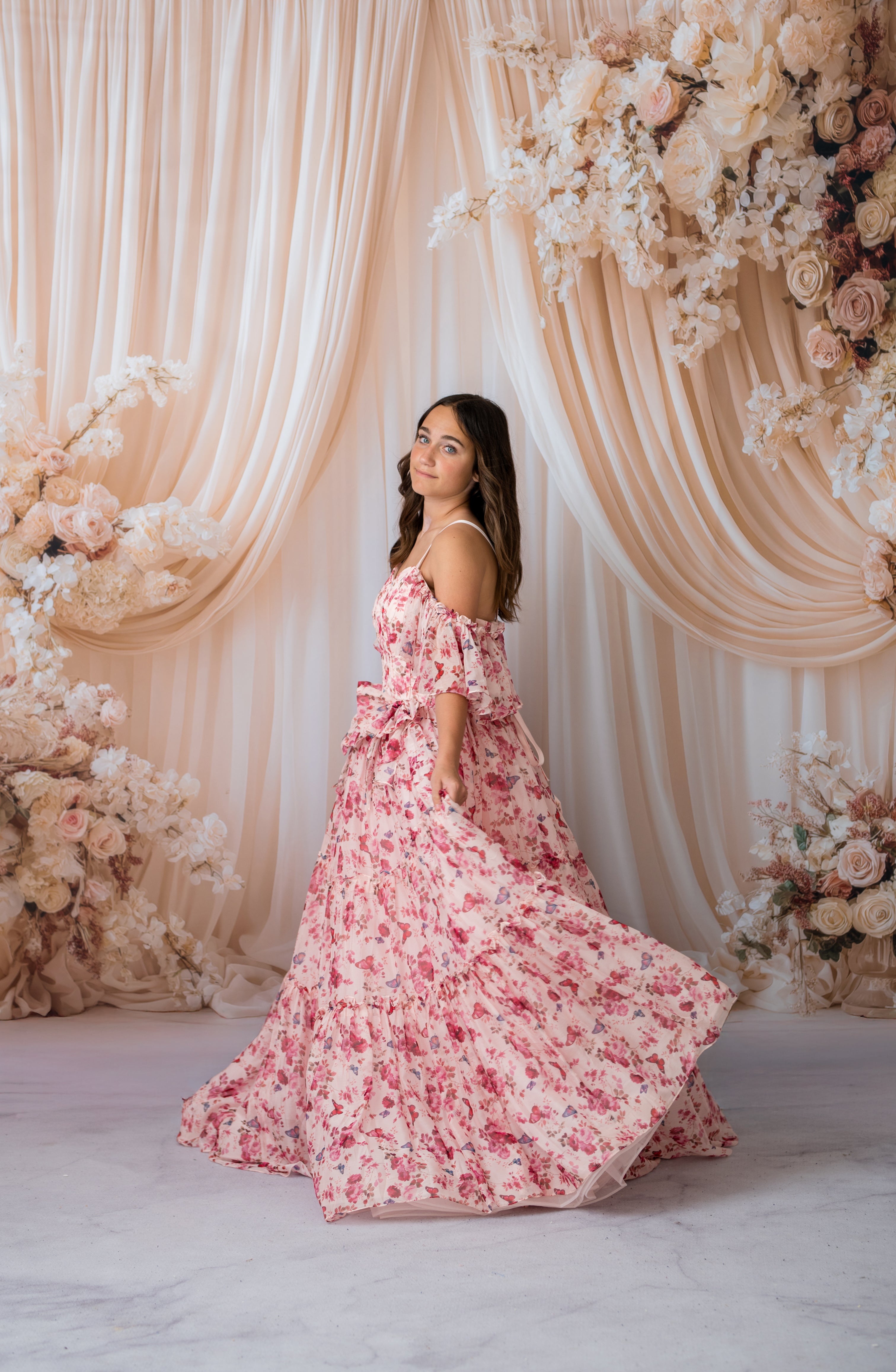 Woman in a pink floral dress standing in front of a decorative floral backdrop.