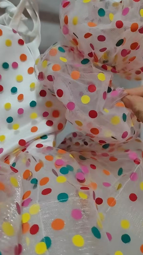 Colorful polka dot baby outfit held by a hand against a white background