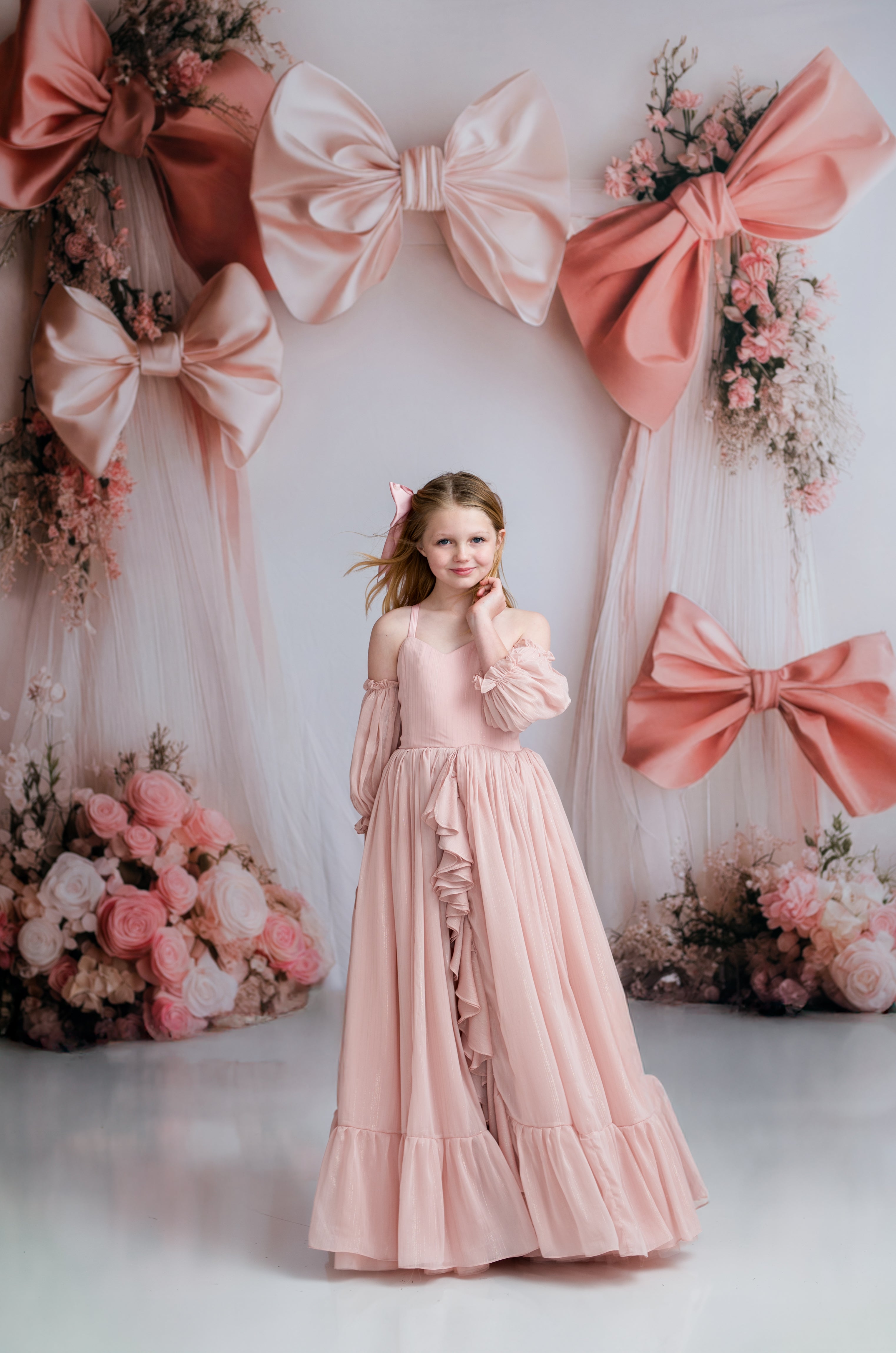 Young girl in a pink dress standing in front of decorative bows and flowers.