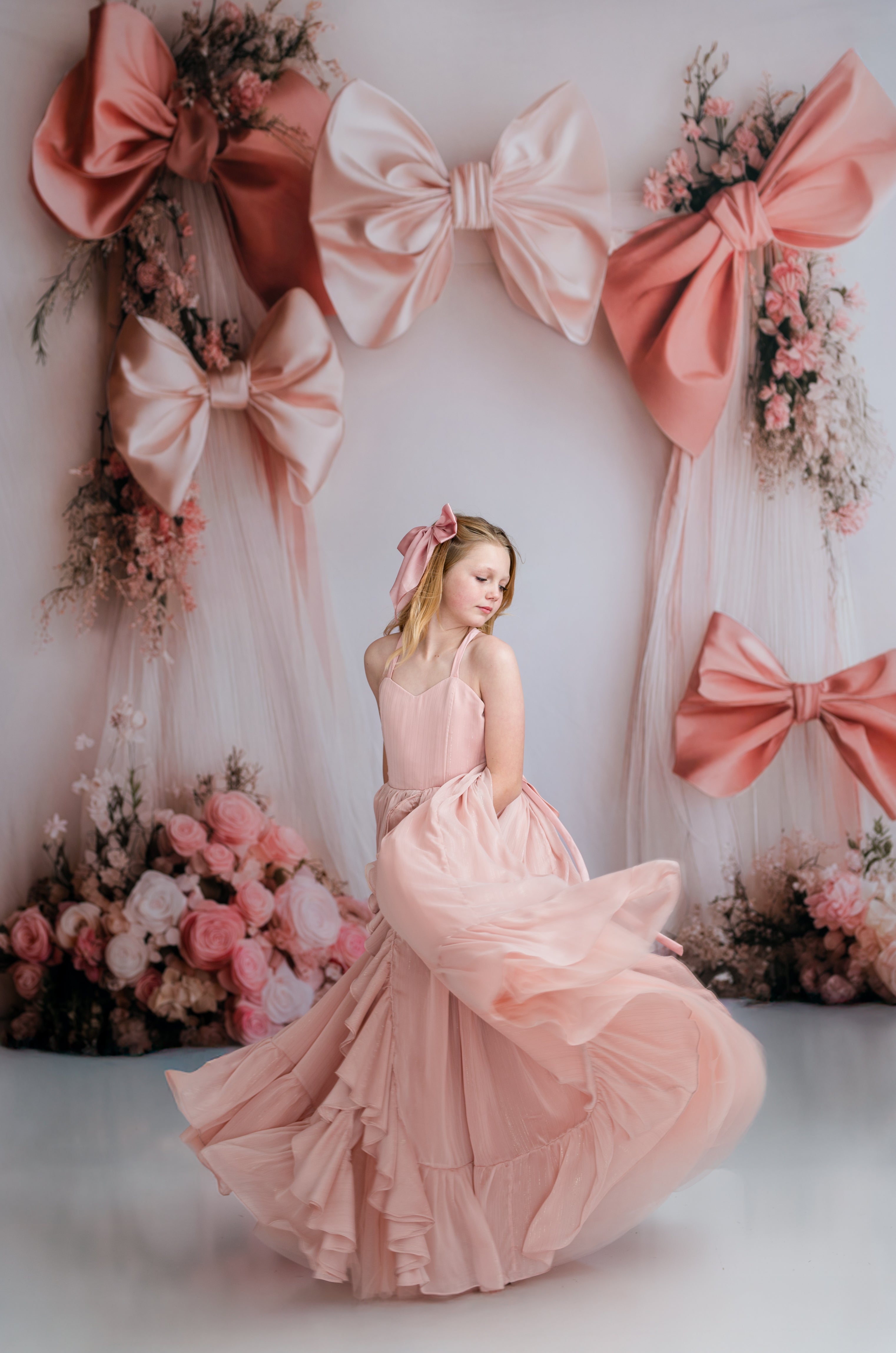 Woman in a pink dress standing in front of decorative bows and flowers.