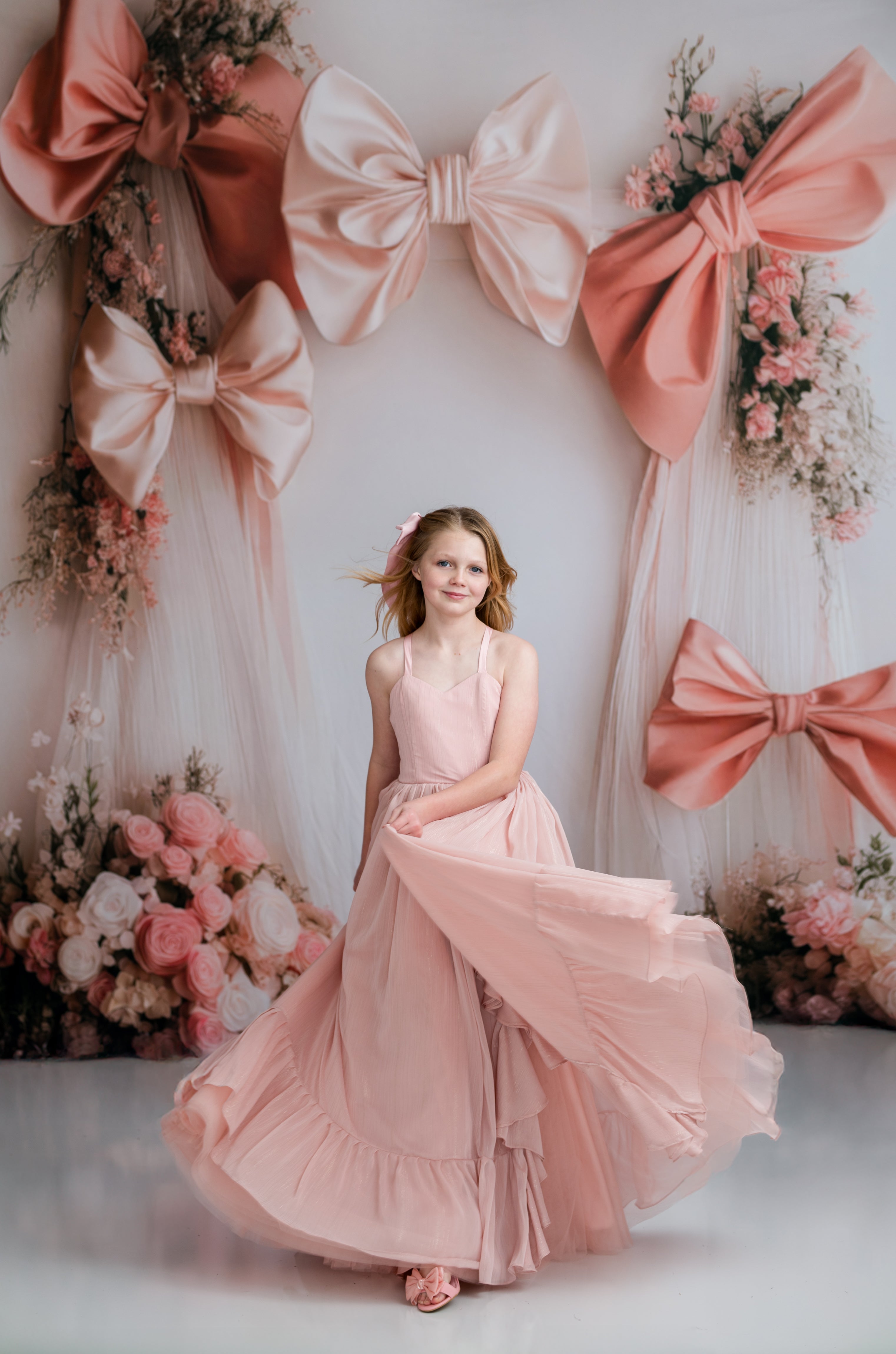 Woman in a pink dress standing in front of decorative bows and flowers.