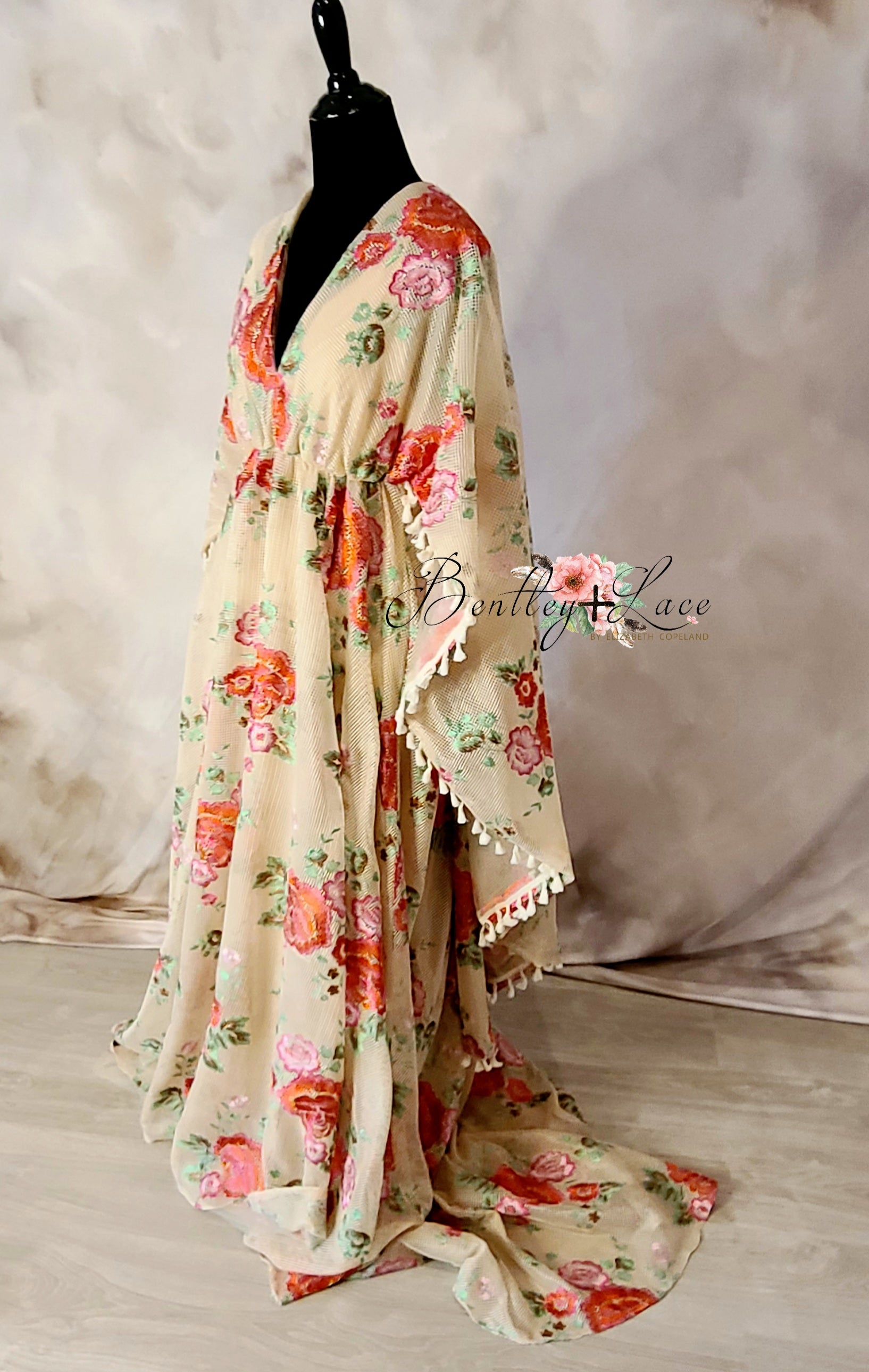A floral gown with a beige color scheme, featuring crochet details and lace embellishments, worn by a mannequin against a neutral background.