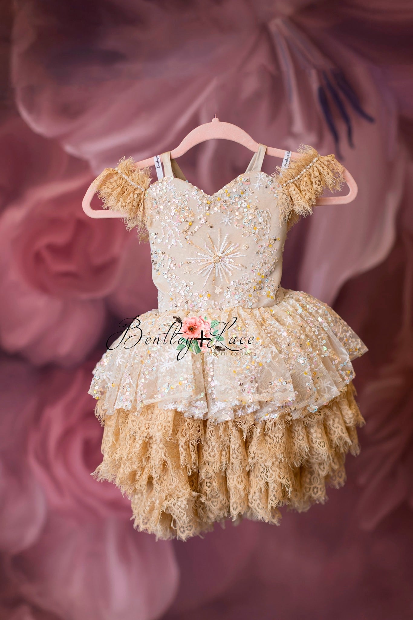 A toddler's vintage petal length dress with lace detail, predominantly in pink and tan colors, displayed on a hanger.