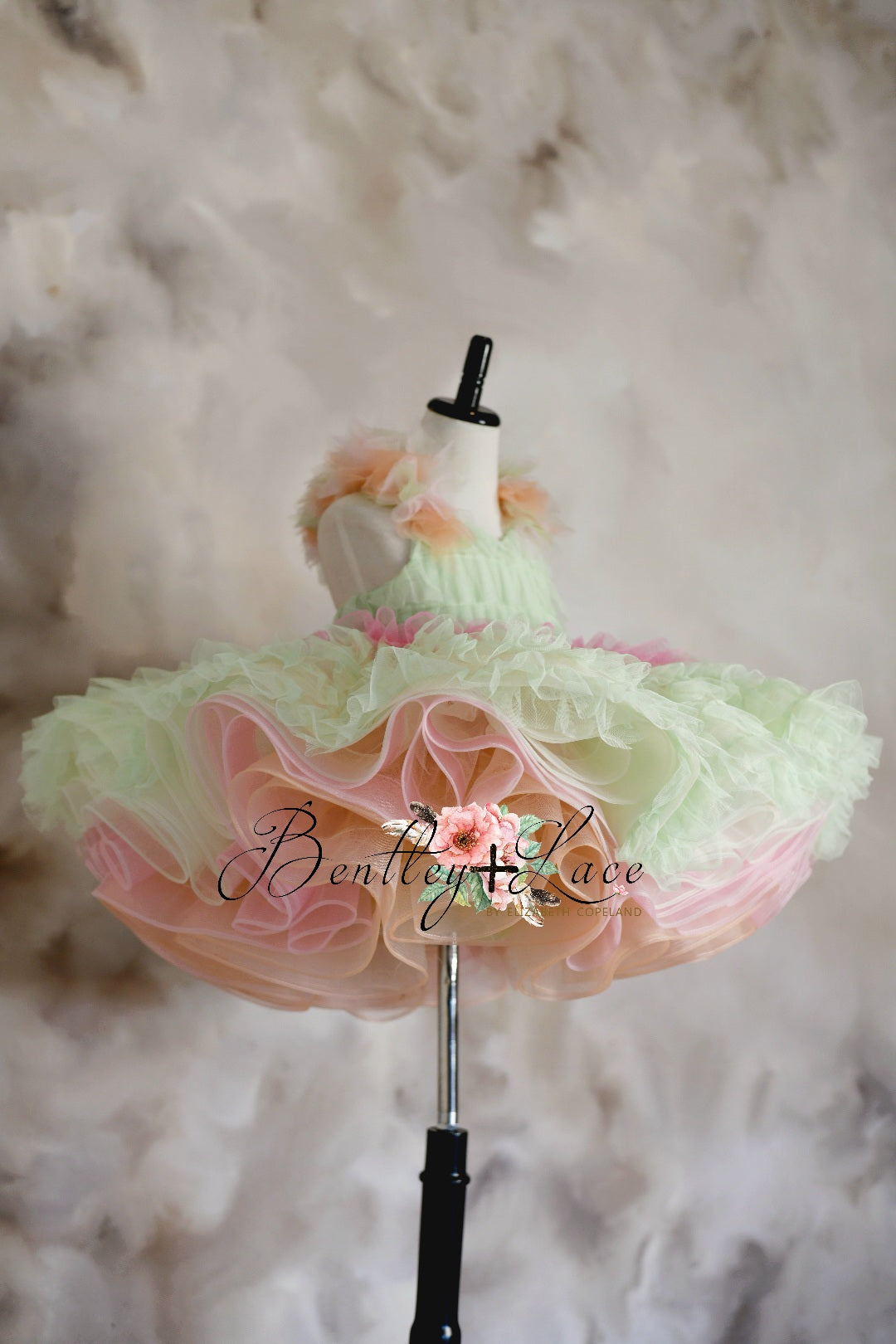 A floral silk fabric dress with a ruffled design and tulle skirt, predominantly in pastel colors, displayed on a mannequin.