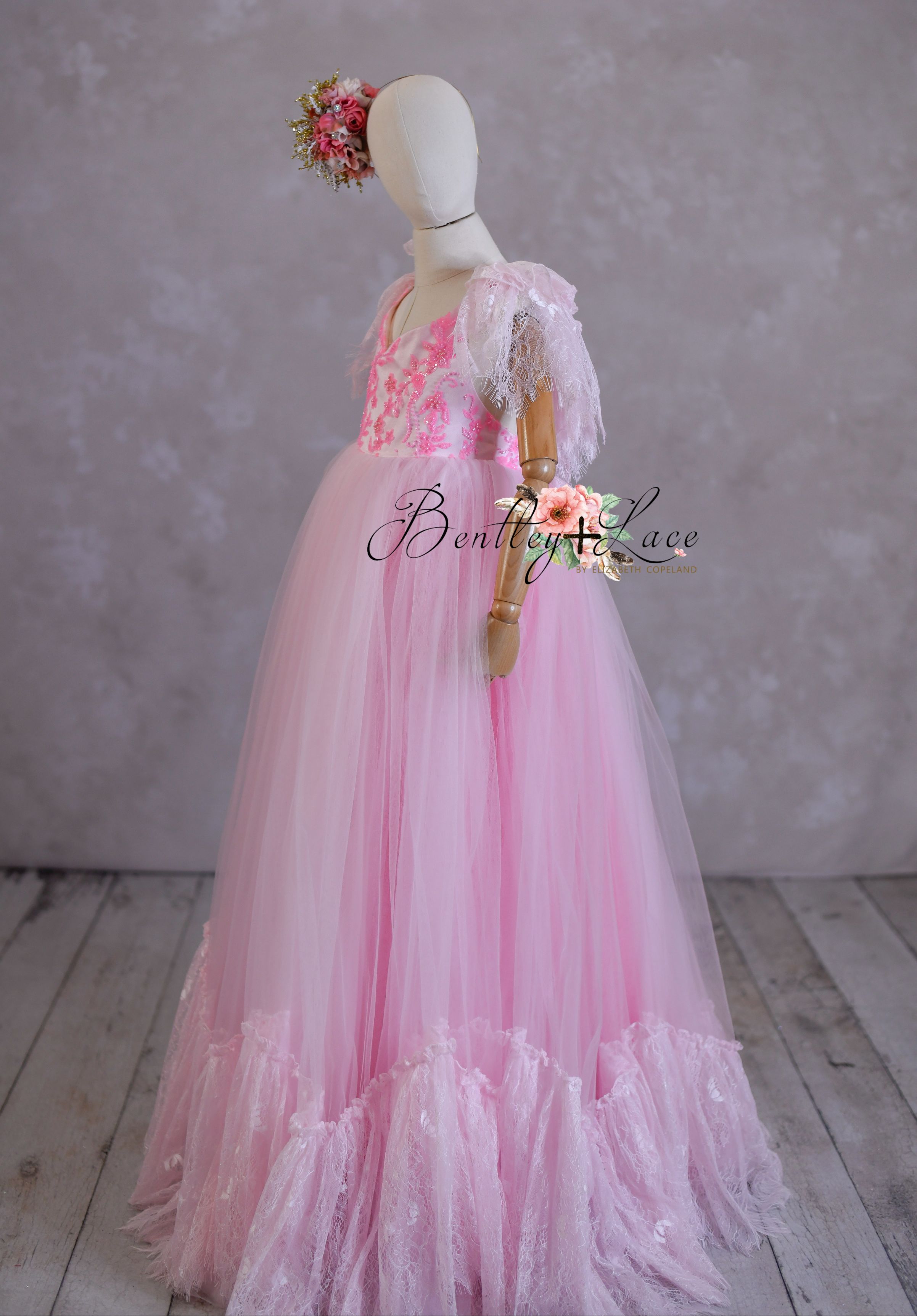 A pink floor-length gown with lace details and a beaded bodice on a mannequin, suitable for a 9-10 year old child.