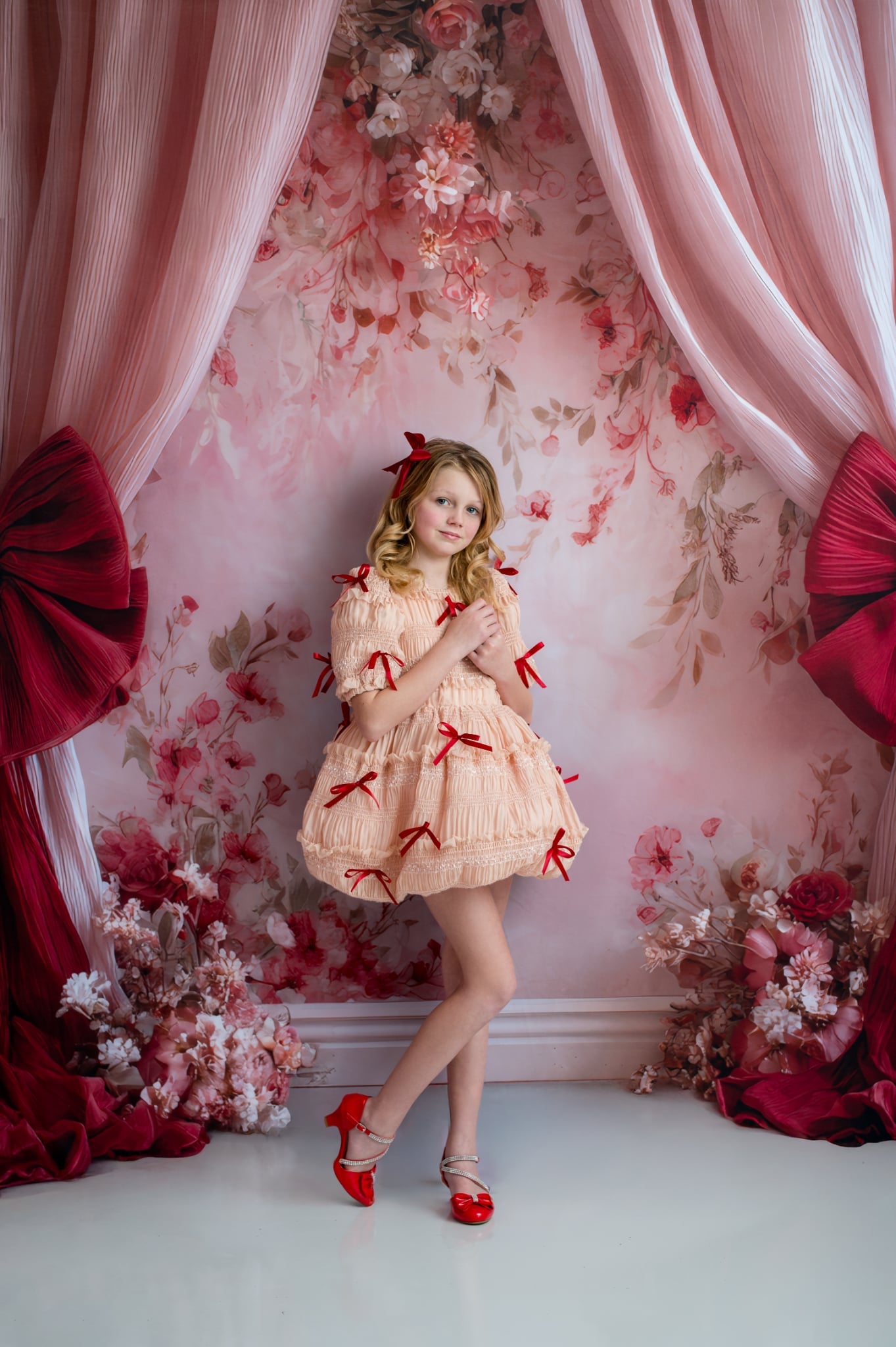 Woman in a decorated room with floral wallpaper, pink curtains, and red bows.