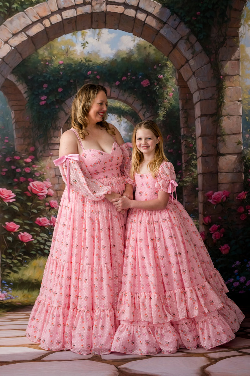 Two women in pink dresses standing under a stone archway with floral decorations.
