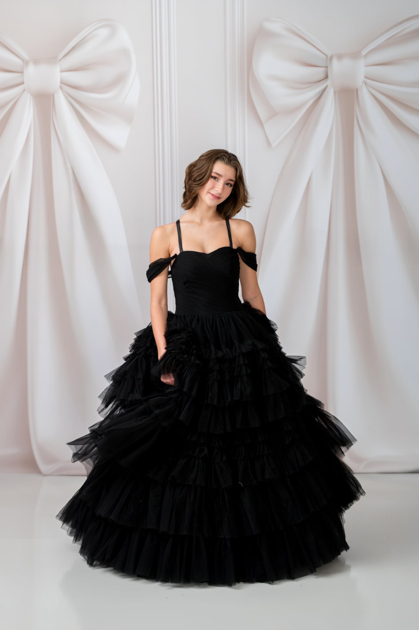 Woman in a black ruffled gown standing against a white wall with large decorative bows.